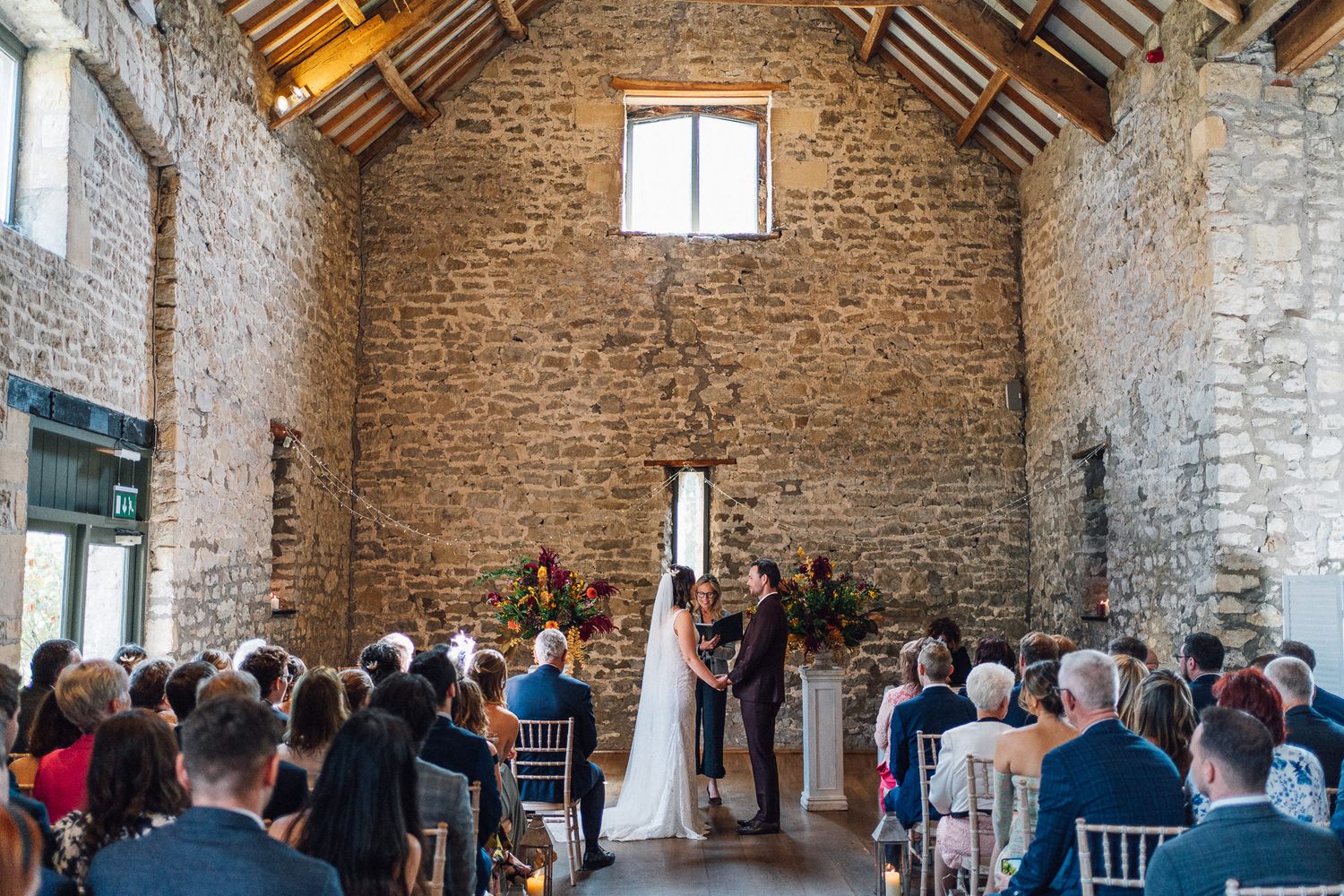 Interior of historic stone barn filled with guests seated in rows for wedding ceremony.
