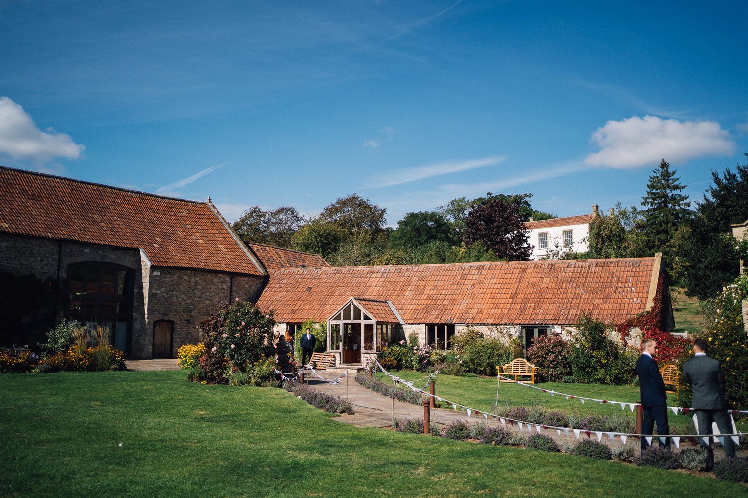 Panoramic view of rustic barn wedding venue with multiple buildings and green lawns under blue sky.