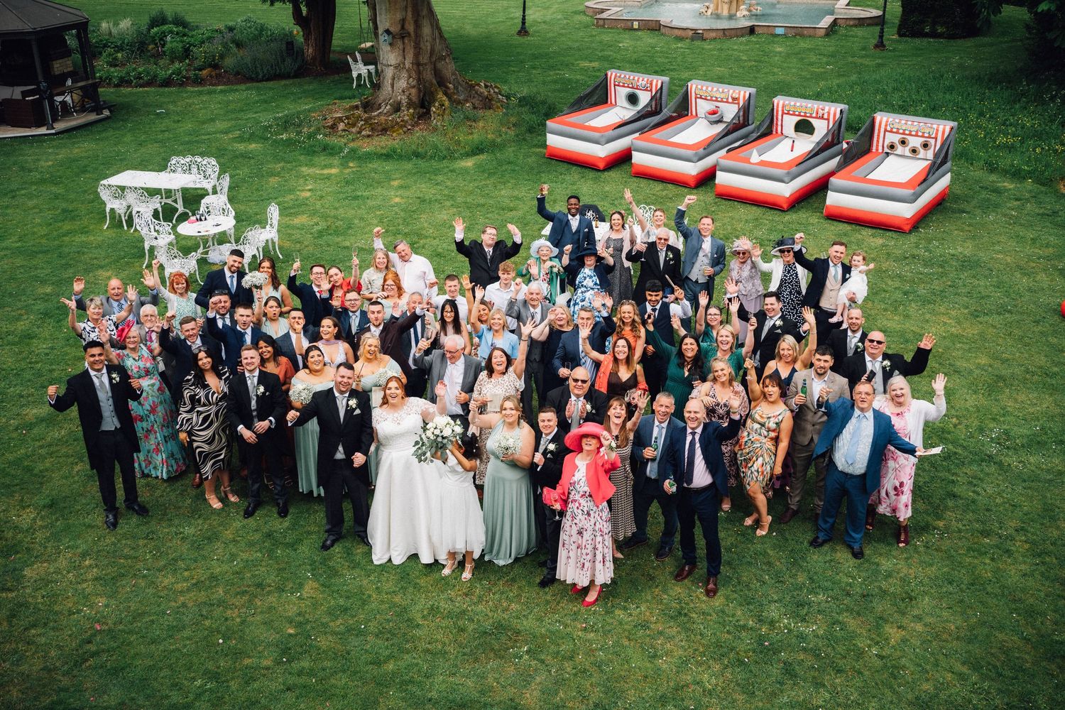 Large group of wedding guests gathered outdoors on a grassy lawn for a celebratory photo.