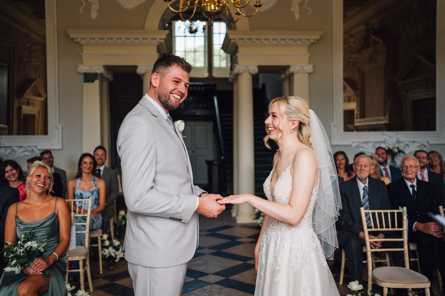 A joyful wedding ceremony takes place in an elegant room with ornate moldings as a couple exchanges rings.
