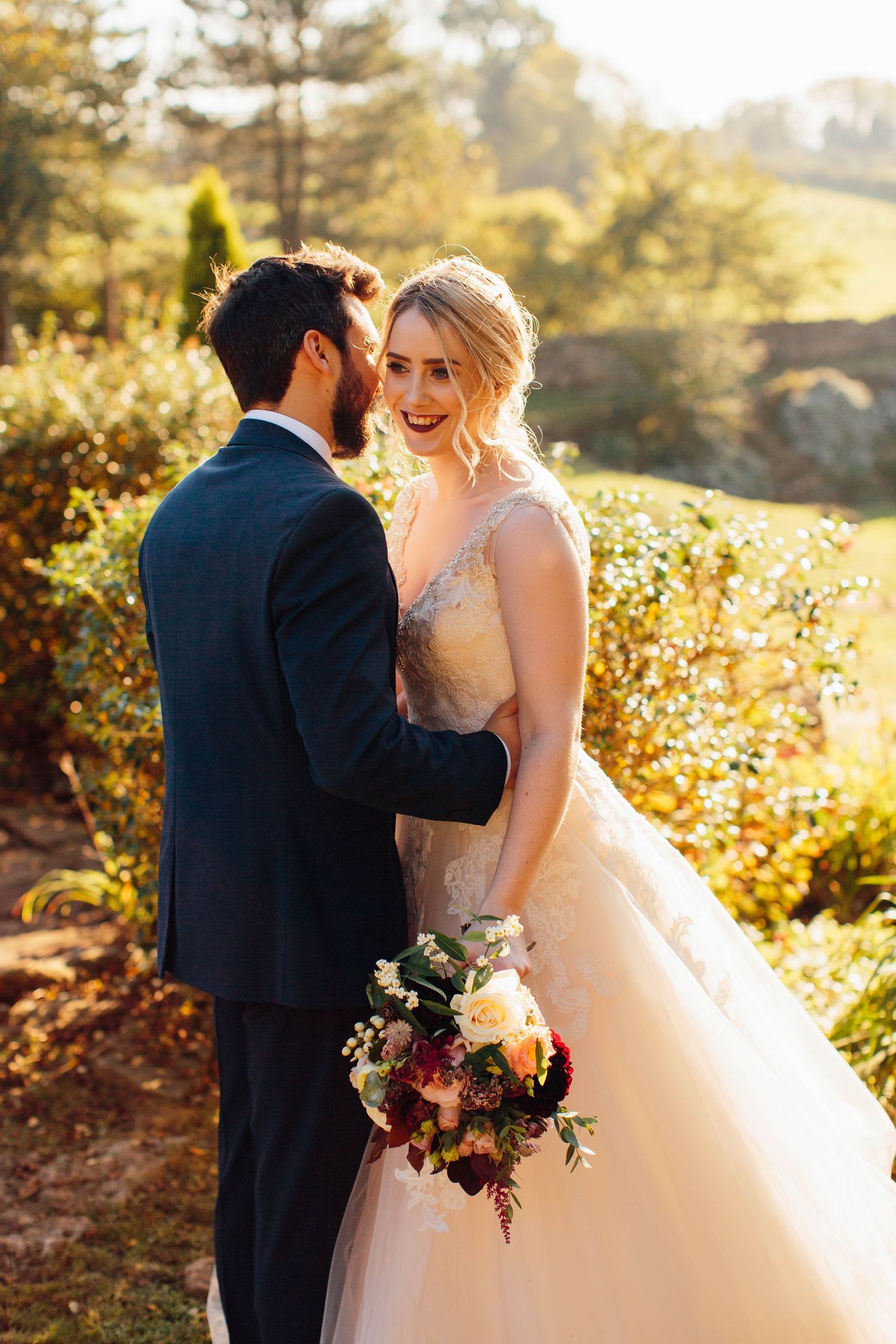 Romantic outdoor autumn wedding portrait with couple embracing among golden foliage.