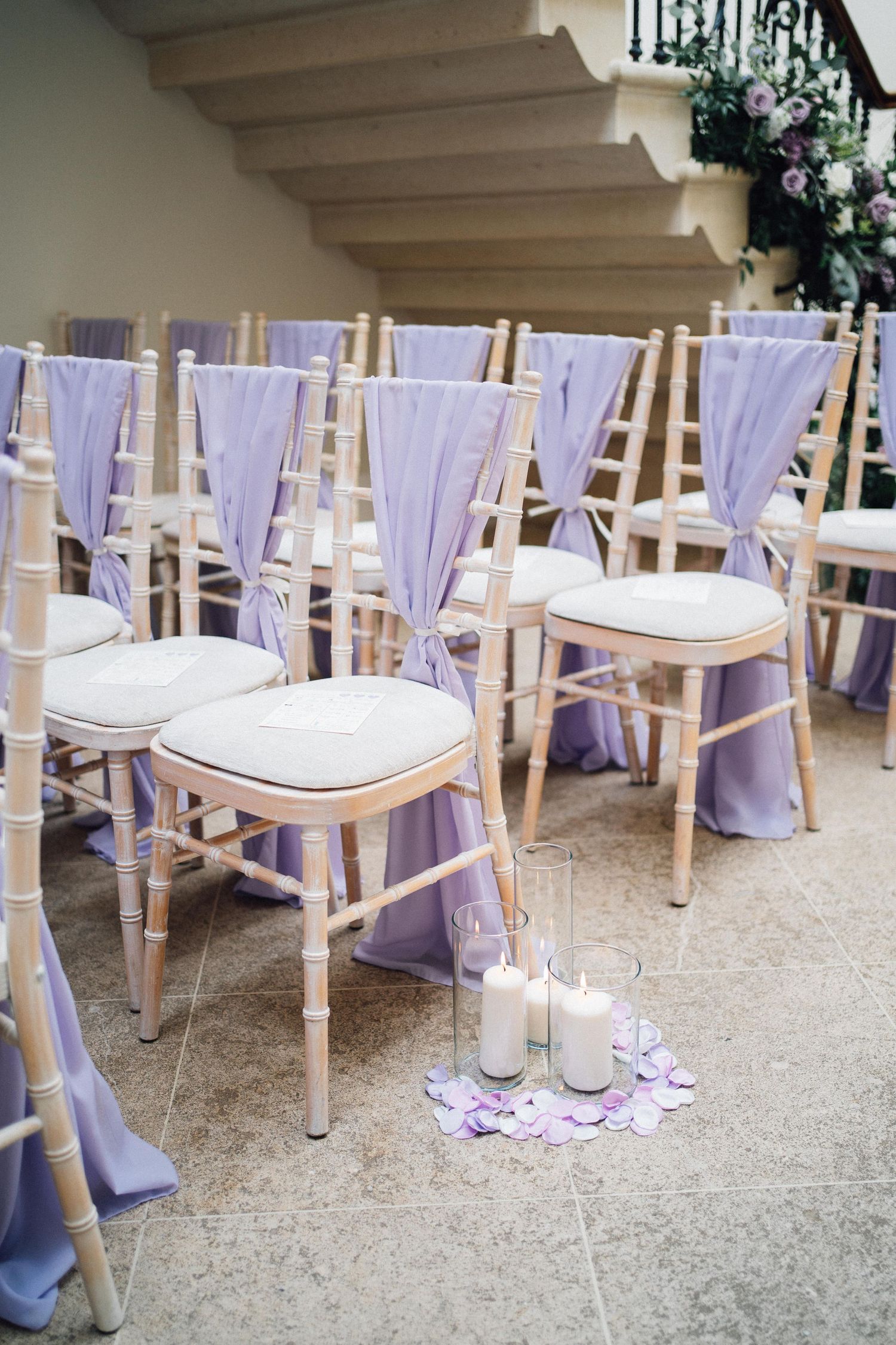 Wedding ceremony chairs decorated with flowing lavender fabric sashes and floral accents in an elegant setup.