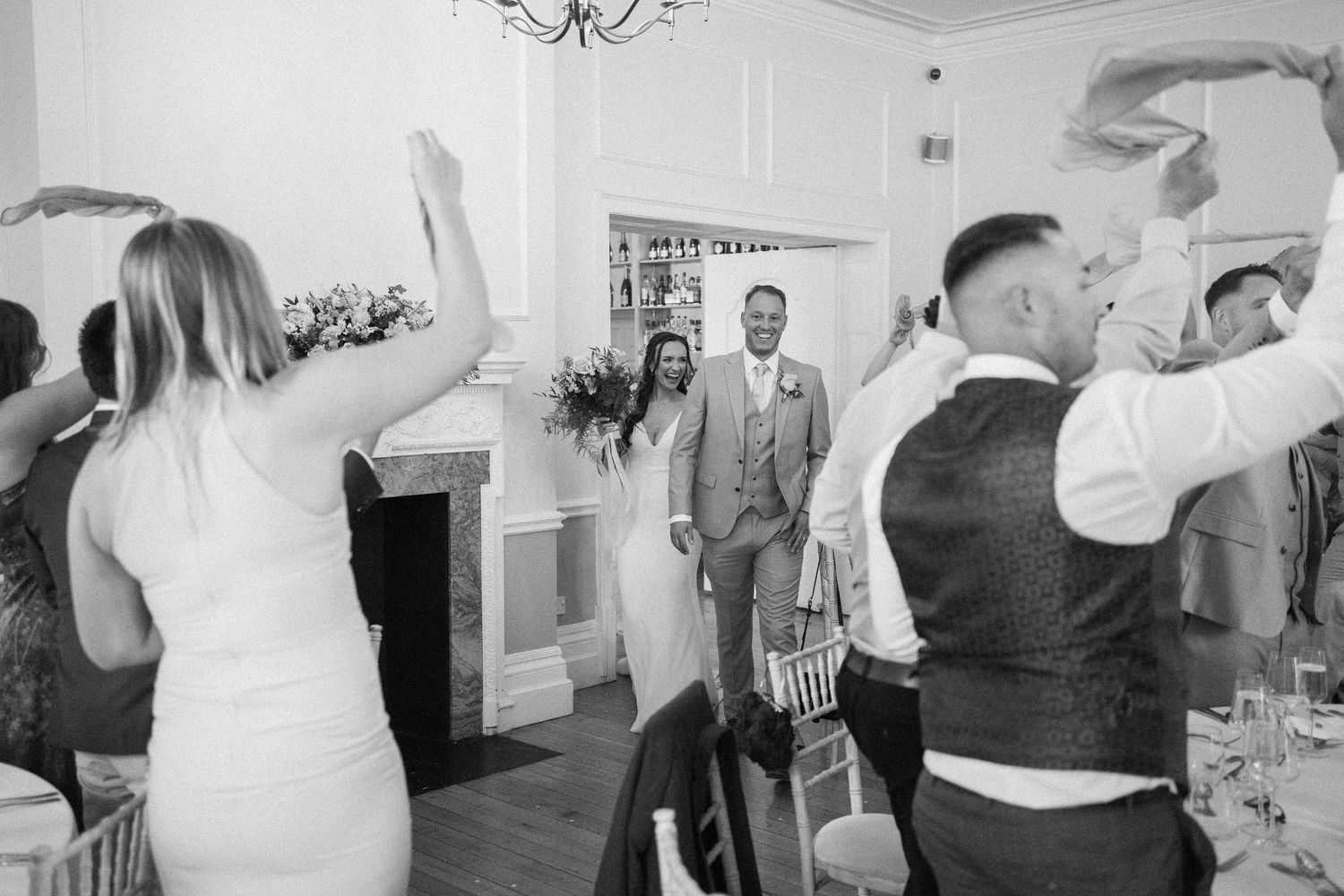 Black and white photo of guests dancing and celebrating at an elegant indoor wedding reception.