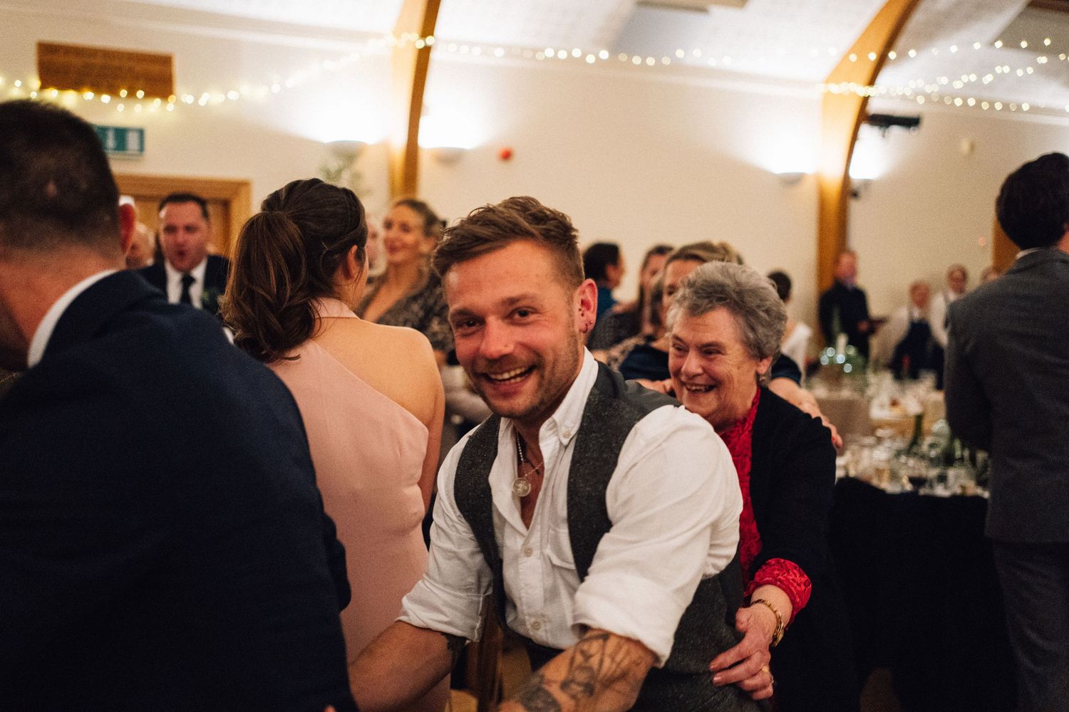 Joyful celebration at a wedding reception with guests mingling and laughing in a bright indoor venue.