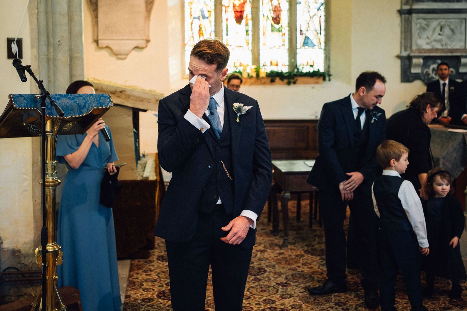 An emotional moment captured during a wedding ceremony inside a church with stained glass windows and traditional decor.