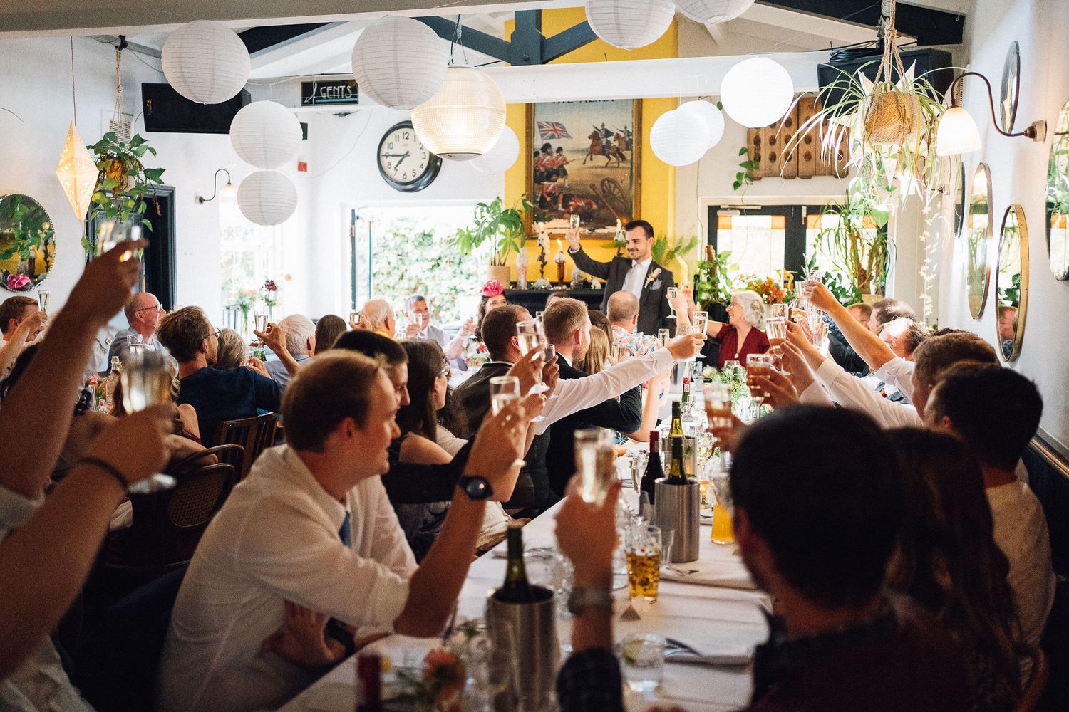 A crowded restaurant interior with people raising their glasses in celebration during a festive gathering.