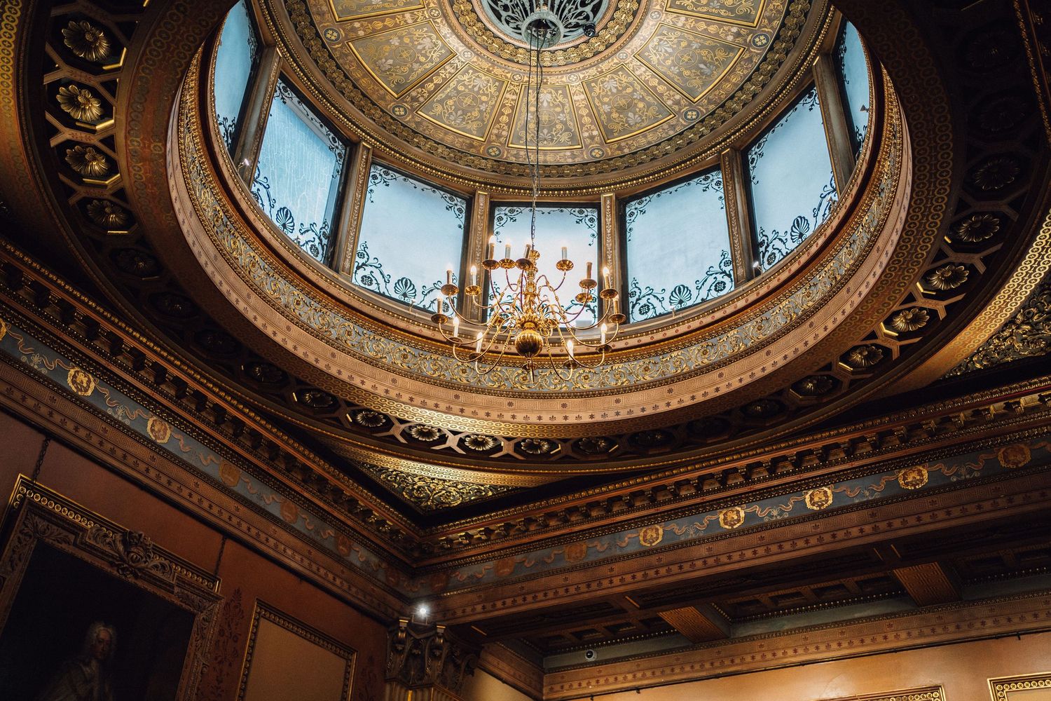 Ornate rotunda ceiling with gold details, stained glass windows, and chandelier in a historic government building.