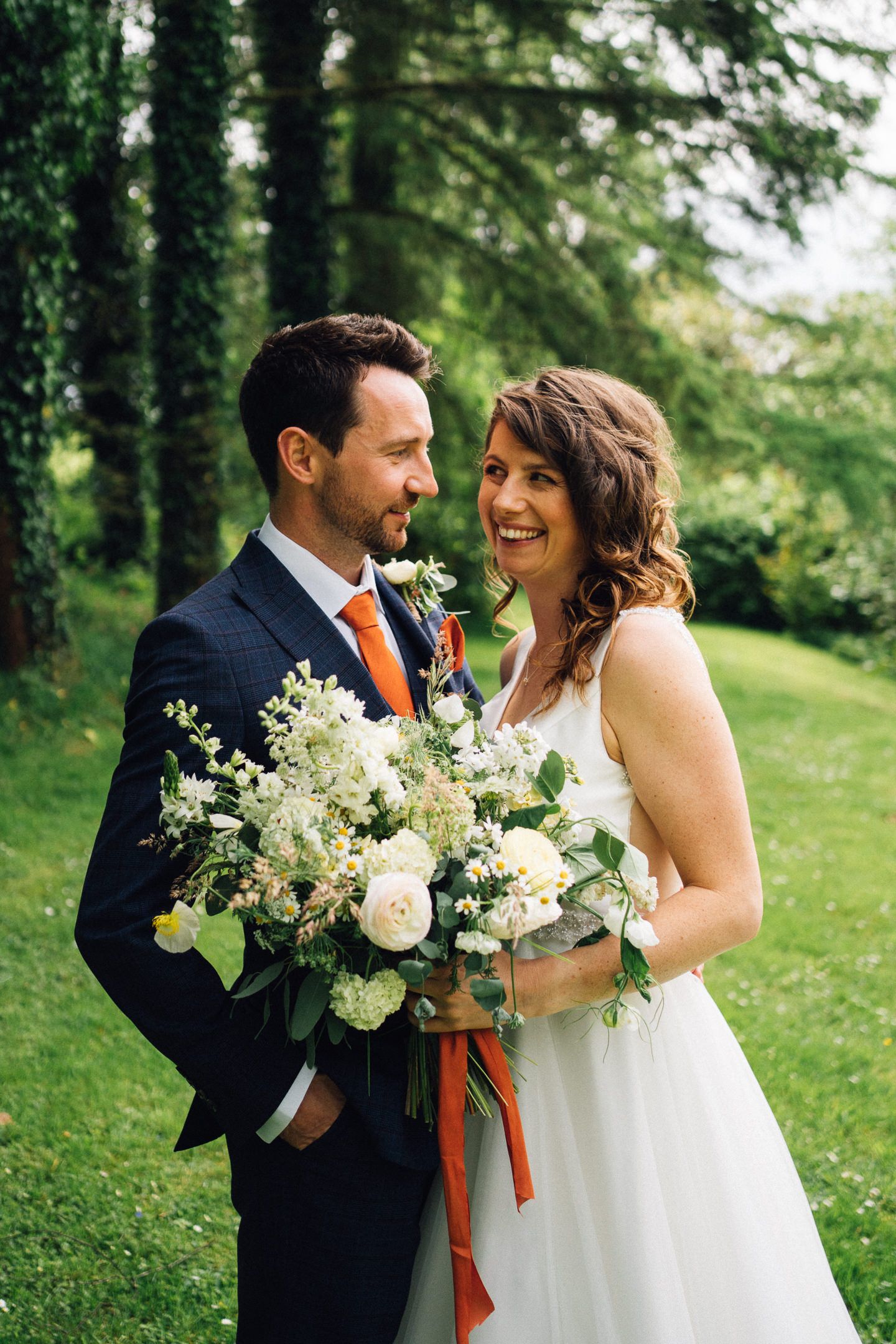 A couple shares a joyful moment while holding floral bouquets in a garden setting.
