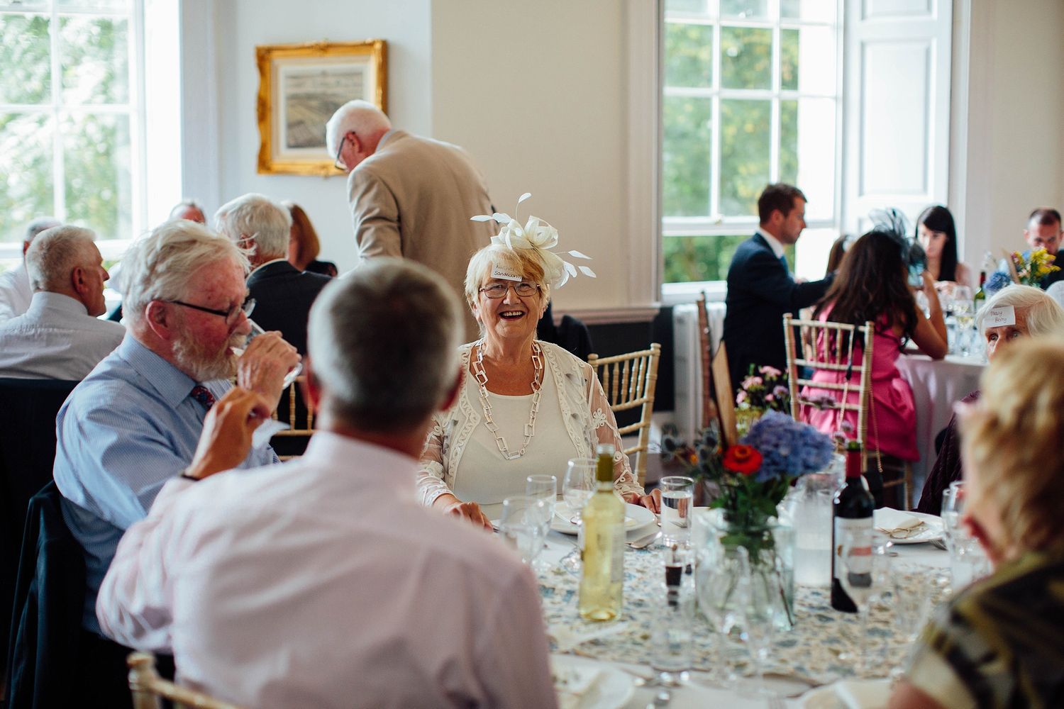Elegant wedding reception dining room with white tablecloths and natural light streaming through windows.