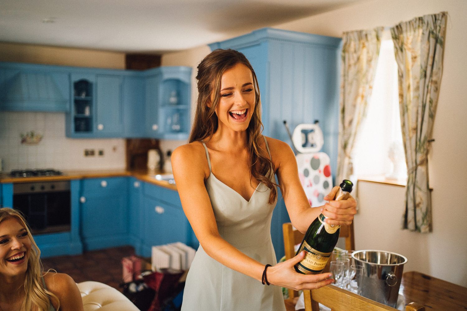 Wedding party members laugh and celebrate while getting ready in a room with blue cabinets.