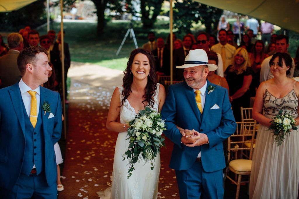 Wedding party and guests gathered under tent with floral decorations.