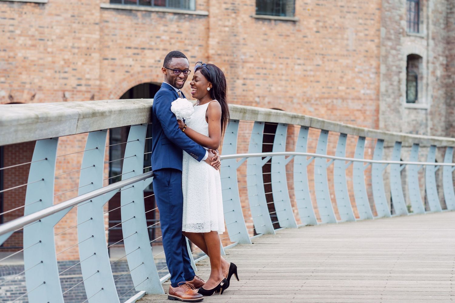 A couple poses romantically on a modern bridge with metal railings.