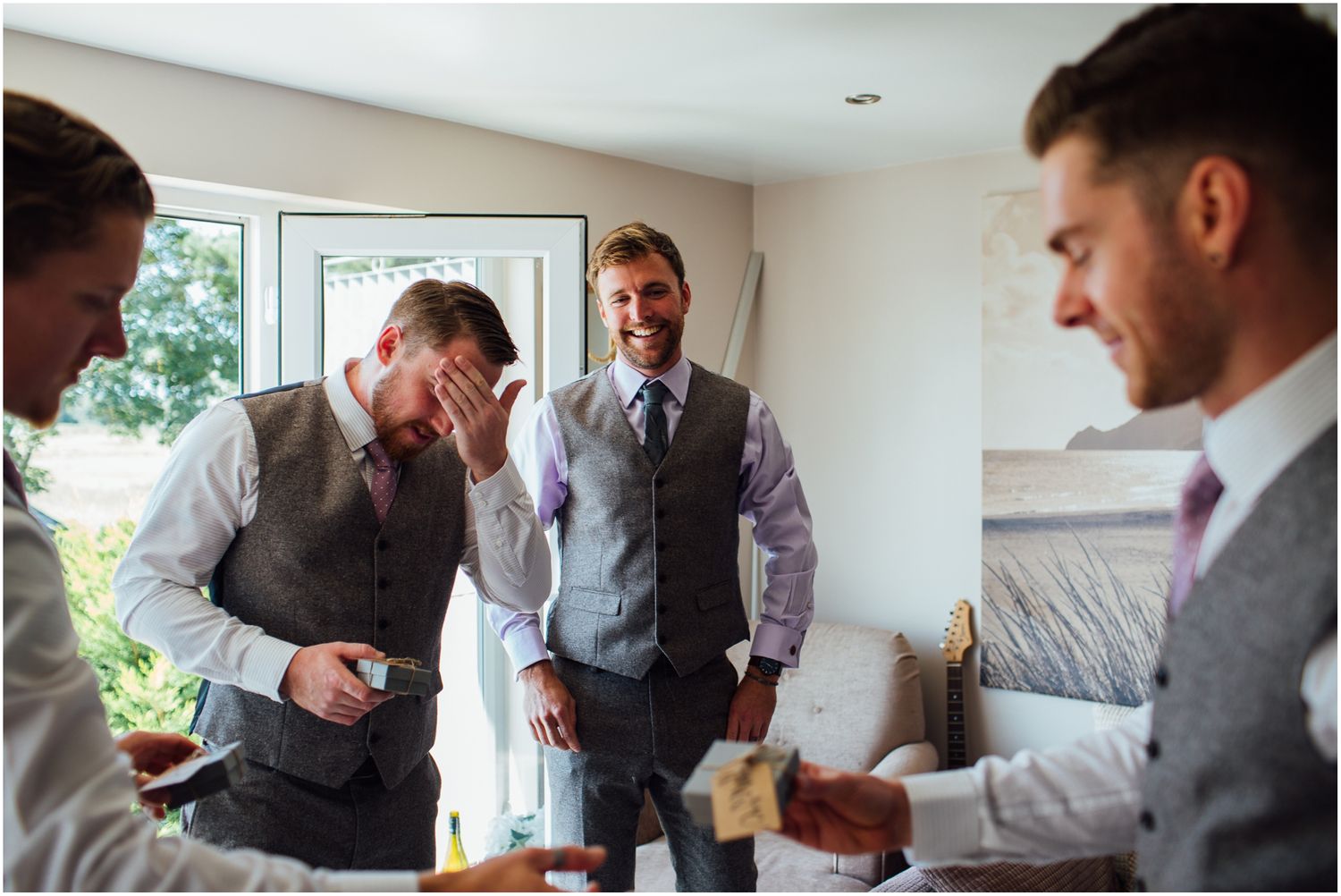 Wedding party members share a laugh while getting ready in a bright room.