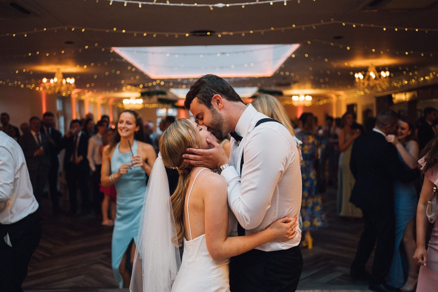 Couples dancing together at an elegant wedding reception under string lights and warm lighting.