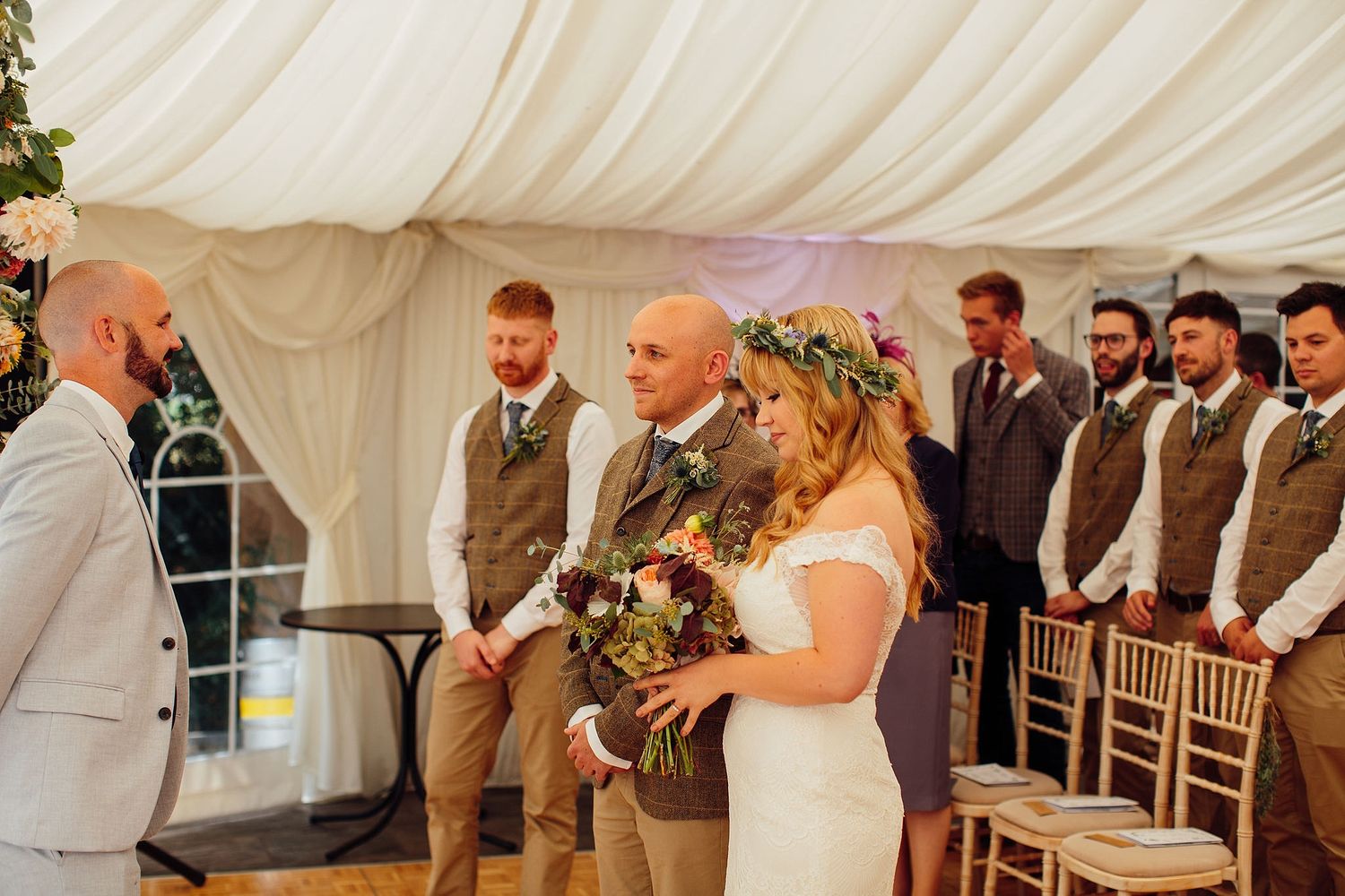 Wedding party and guests celebrating under a white marquee tent with elegant decor.