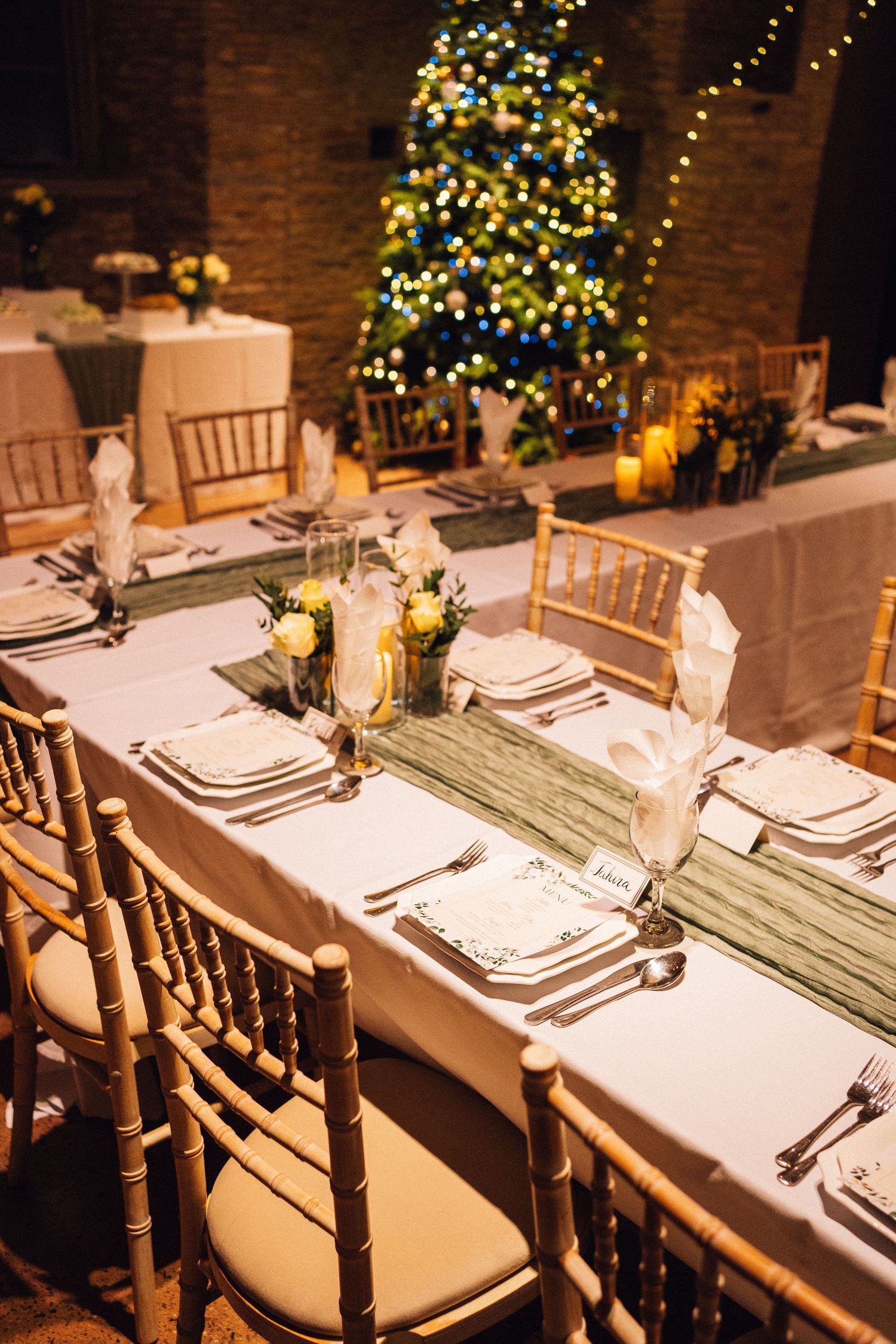 Elegant table settings with white linens and wooden chairs in a rustic venue with twinkling lights.