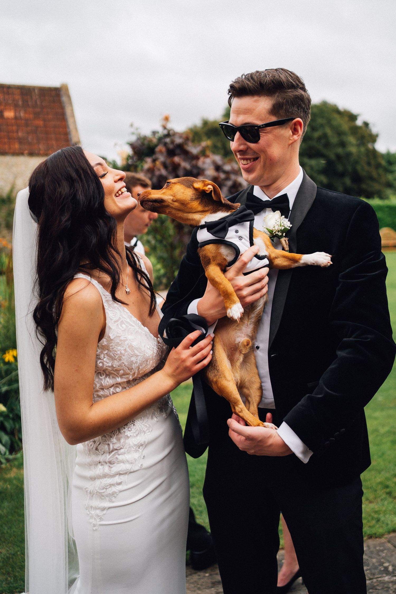 A couple in wedding attire shares joyful moments with their playful dog during an outdoor photo session.