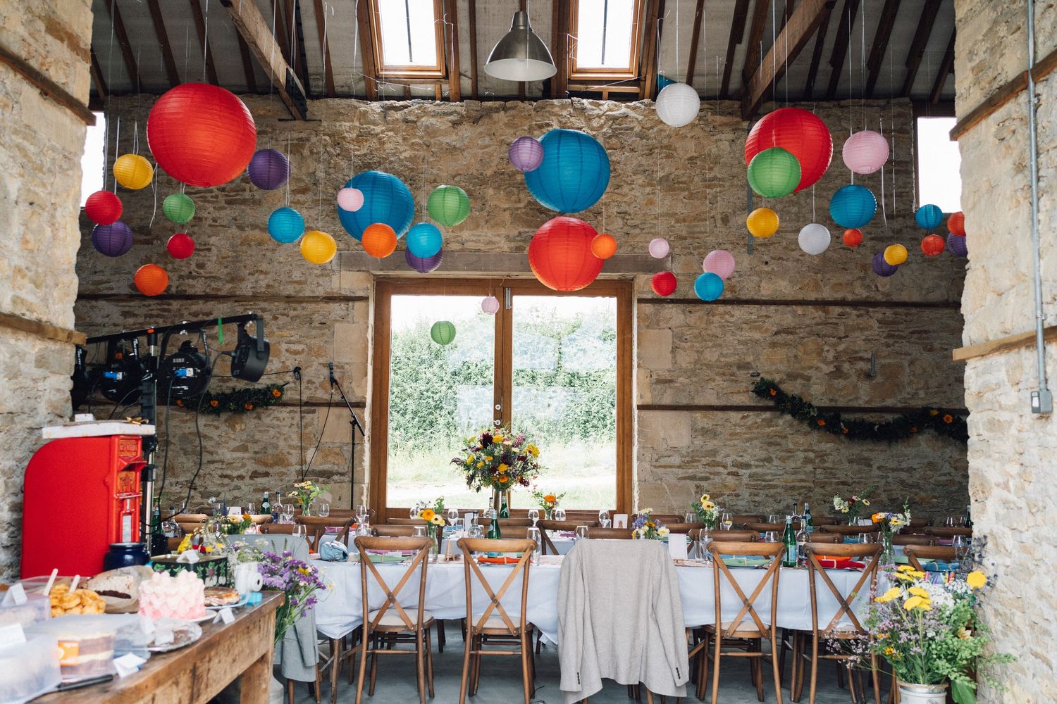 Interior view of a rustic stone barn decorated with vibrant hanging lanterns and table settings.