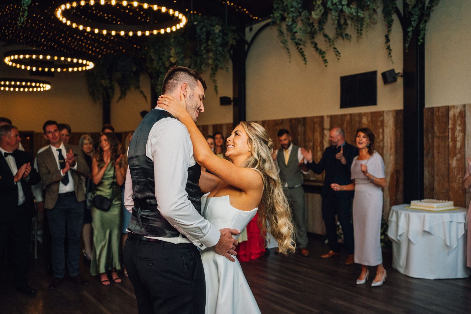 Wedding couple performs romantic dance moves in an elegantly lit reception venue with guests watching.