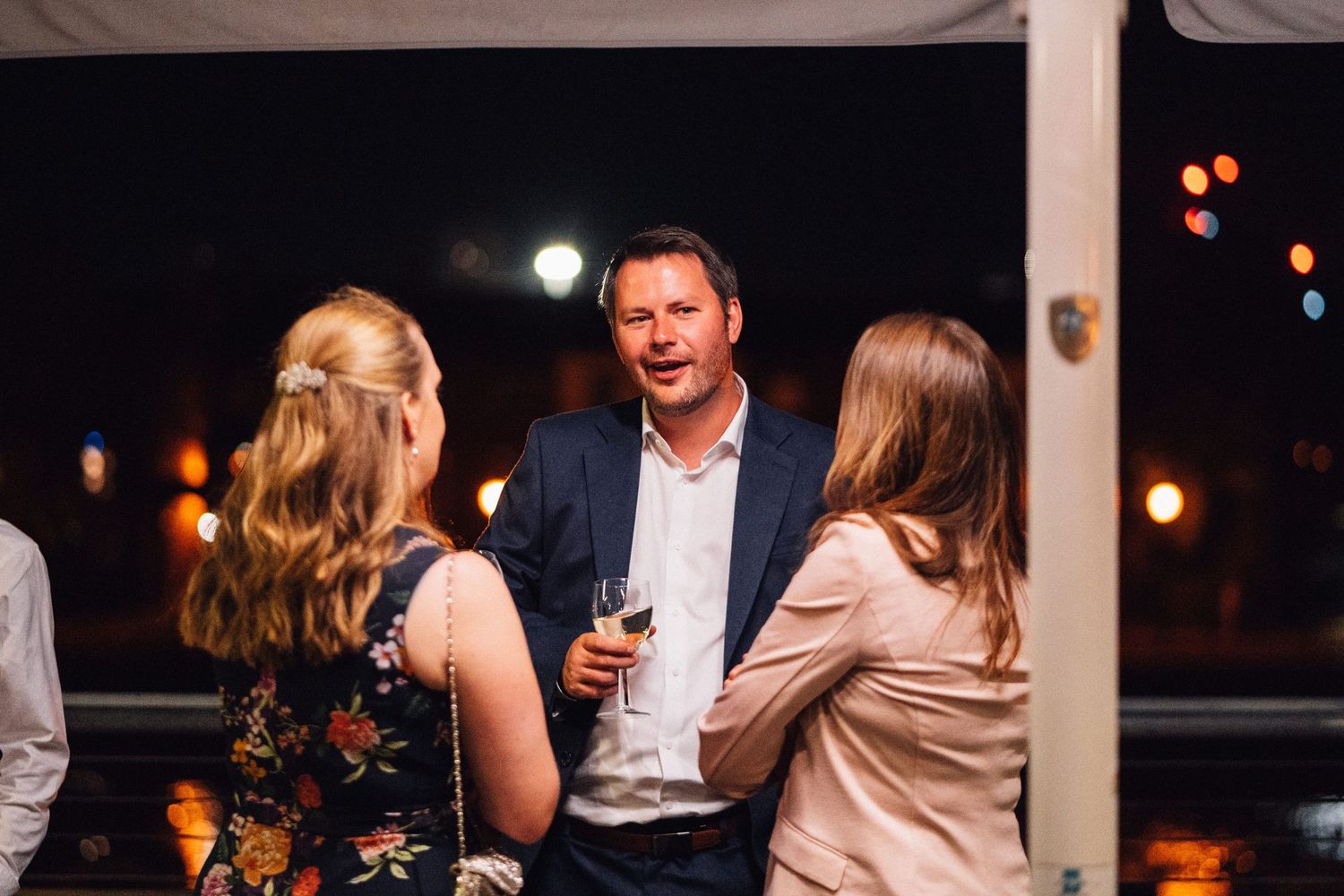 People gathered at an evening dinner party with ambient lighting and wine glasses on wooden tables.