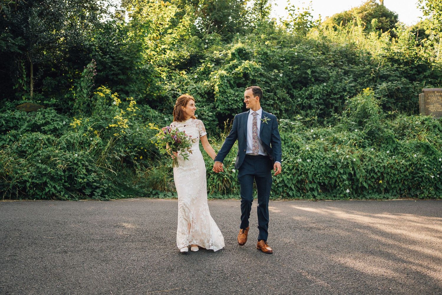 Couple takes romantic walk along garden path during sunset wedding photoshoot.
