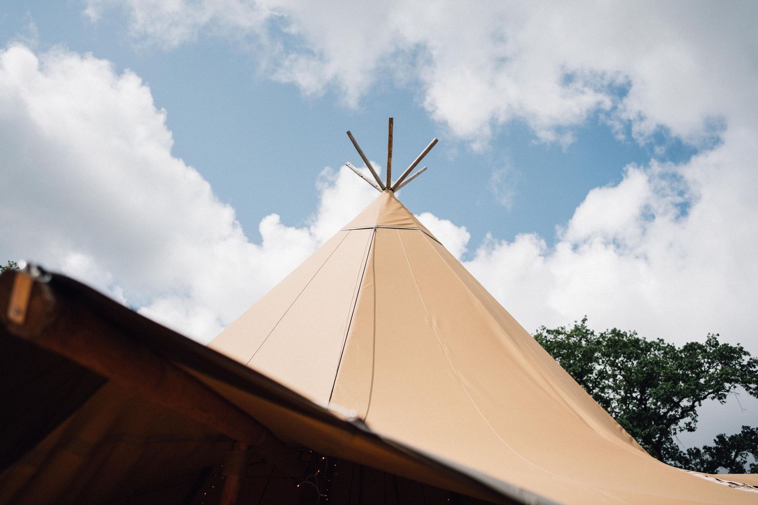 Large beige tipi tents against a blue sky with white fluffy clouds.