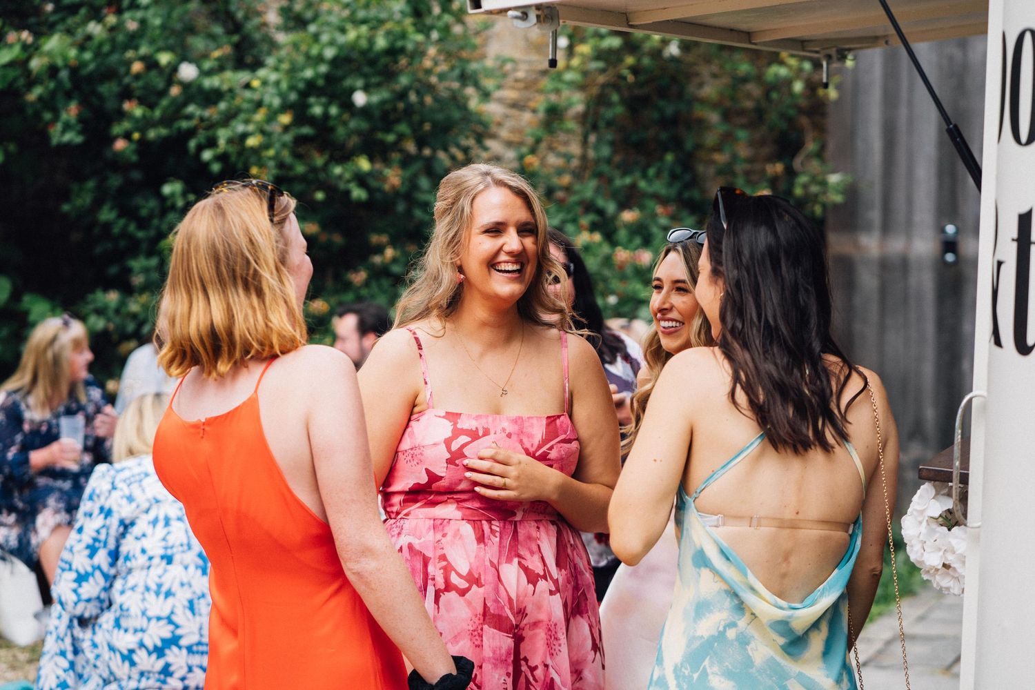 Guests in colorful summer dresses socialize at an outdoor wedding reception.