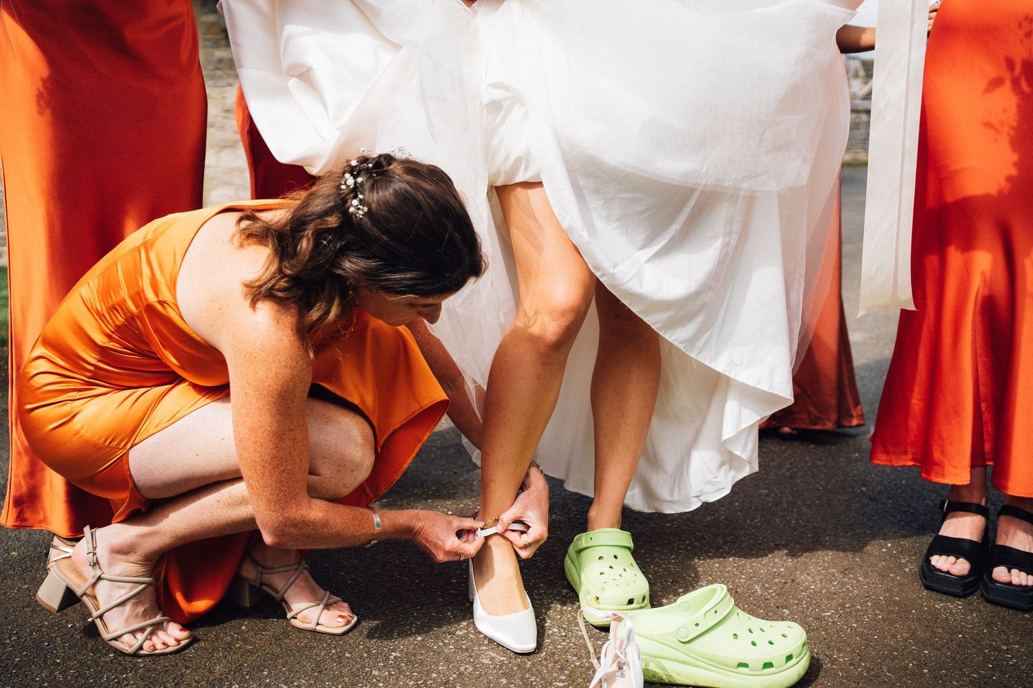 Bridesmaids in bright orange dresses adjusting their shoes before the ceremony.
