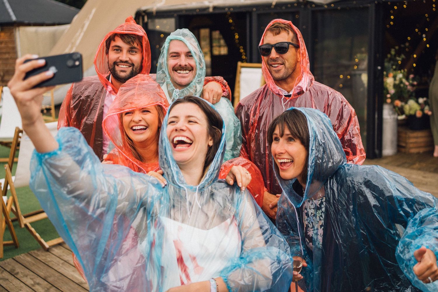 Friends in colorful rain ponchos taking selfies and laughing together at an outdoor event.
