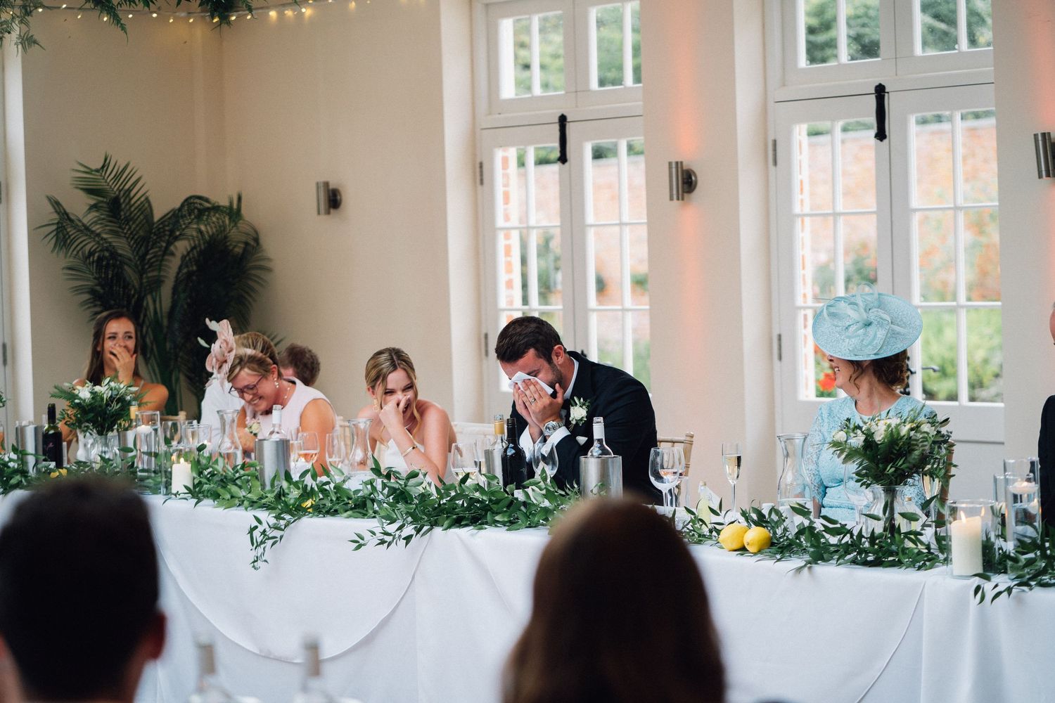Wedding reception venue decorated with string lights and greenery features a long table setup for an elegant celebration.