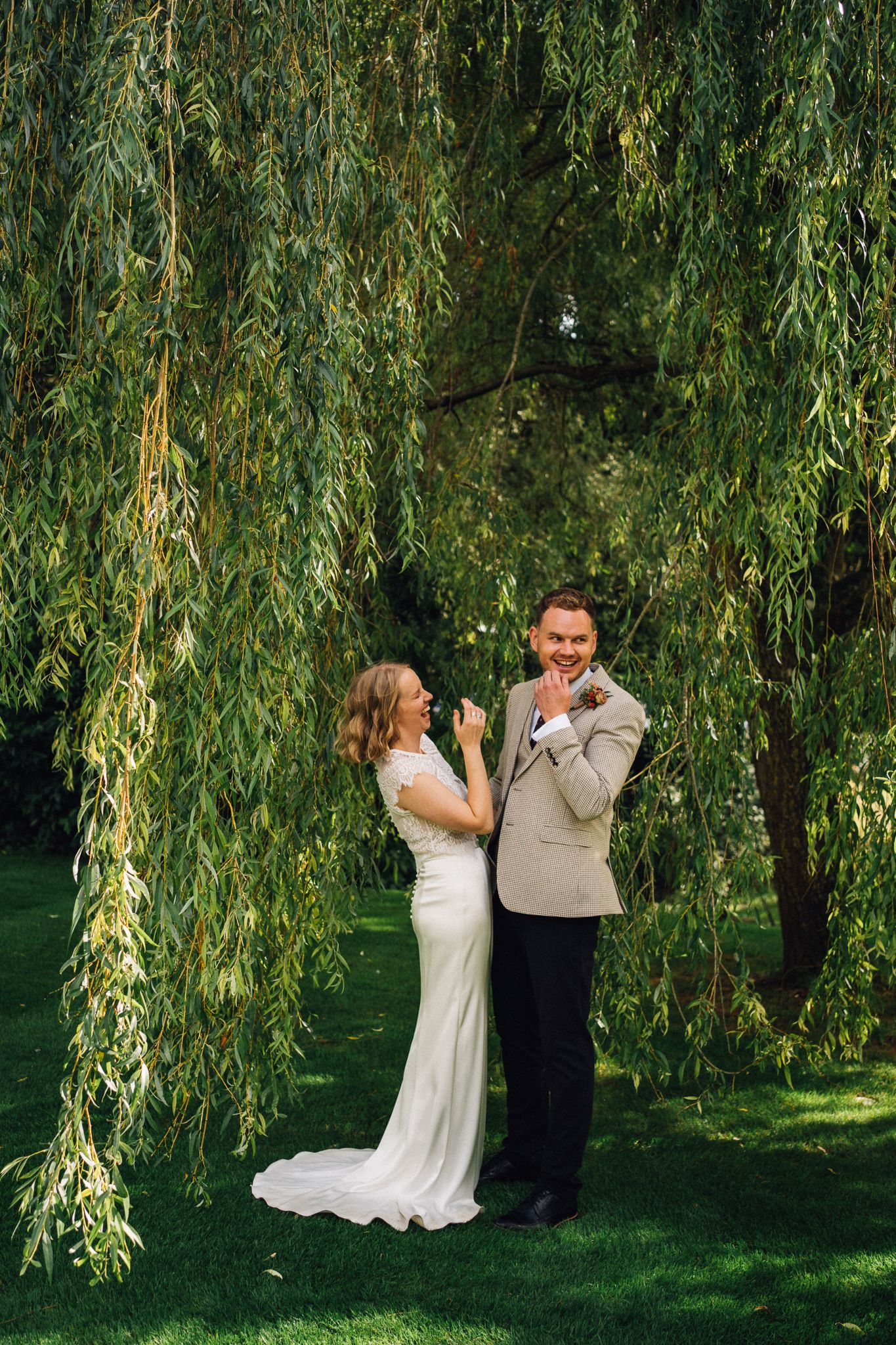 Wedding couple shares intimate moments under drooping willow tree branches in a lush garden setting.