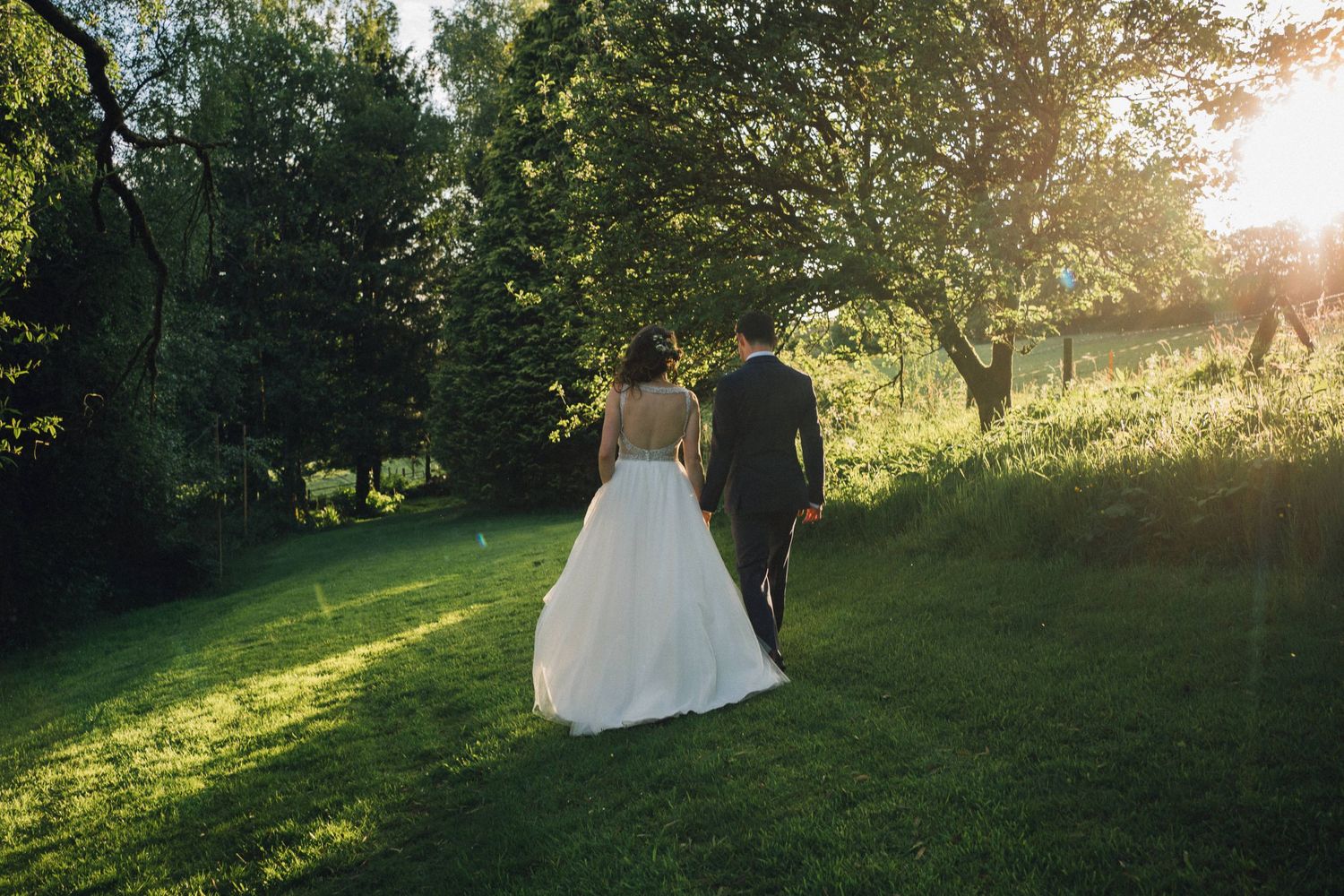 A bride in a white wedding dress stands in a sunlit garden during golden hour creating a romantic silhouette.