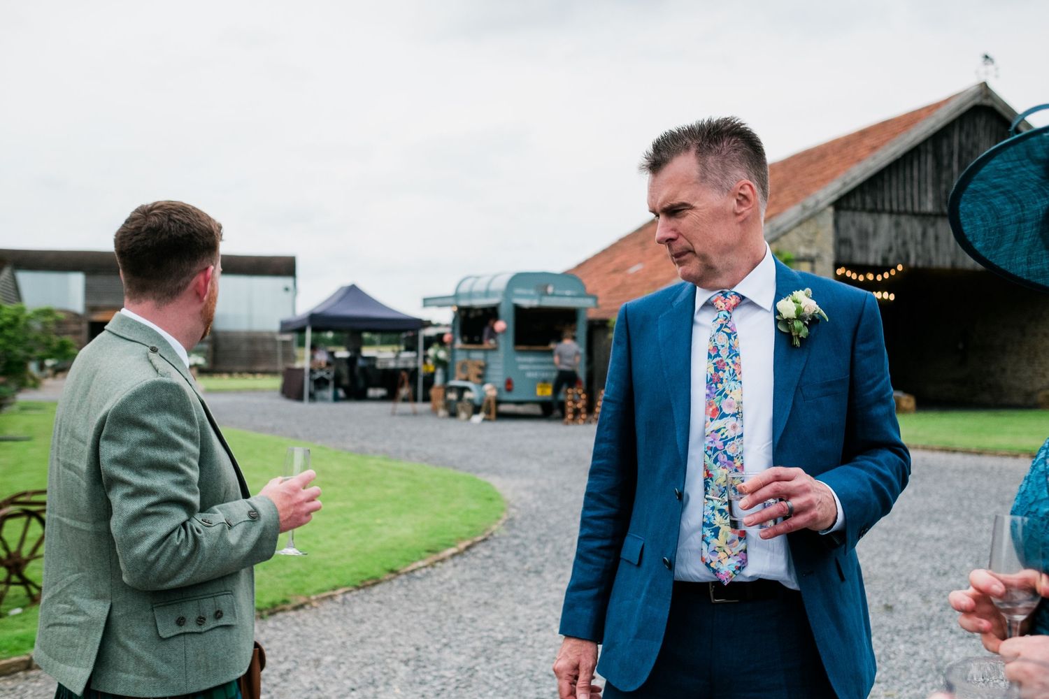 Guests mingling at an outdoor event with rustic barn and gravel path in background.