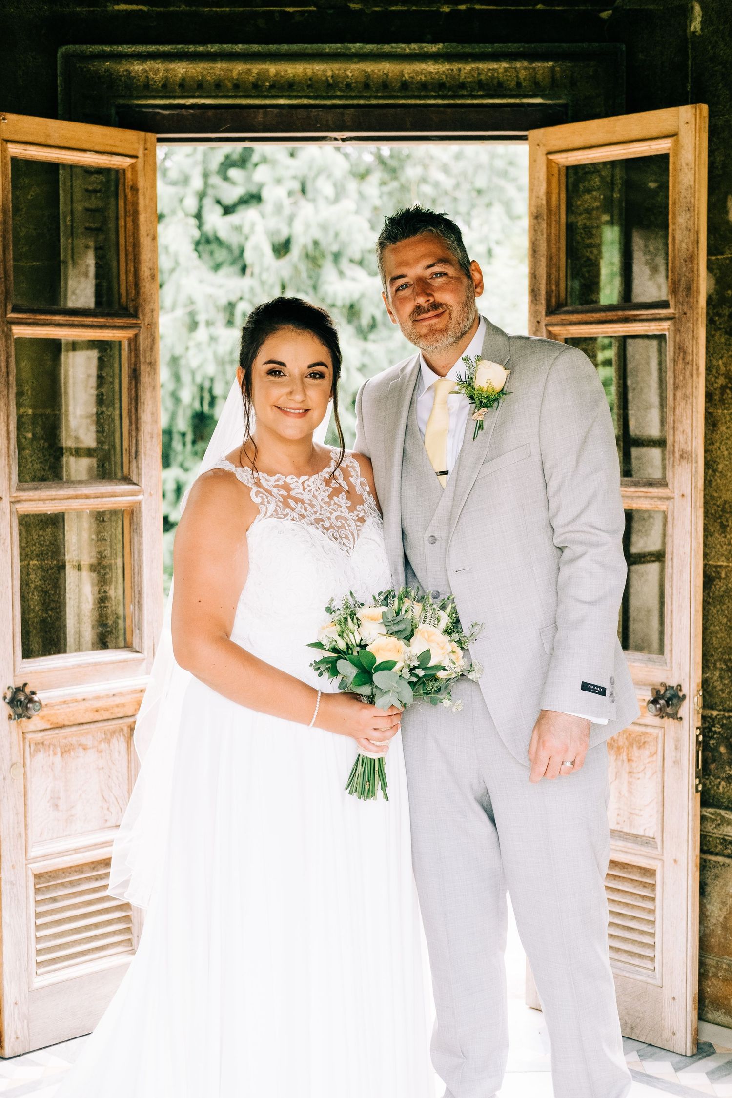 Wedding couple poses in front of wooden doors in natural sunlight.