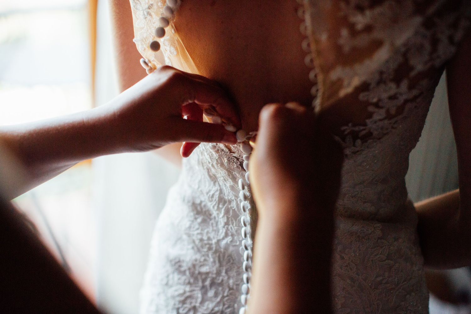 Close-up details of a white lace wedding dress being fastened.