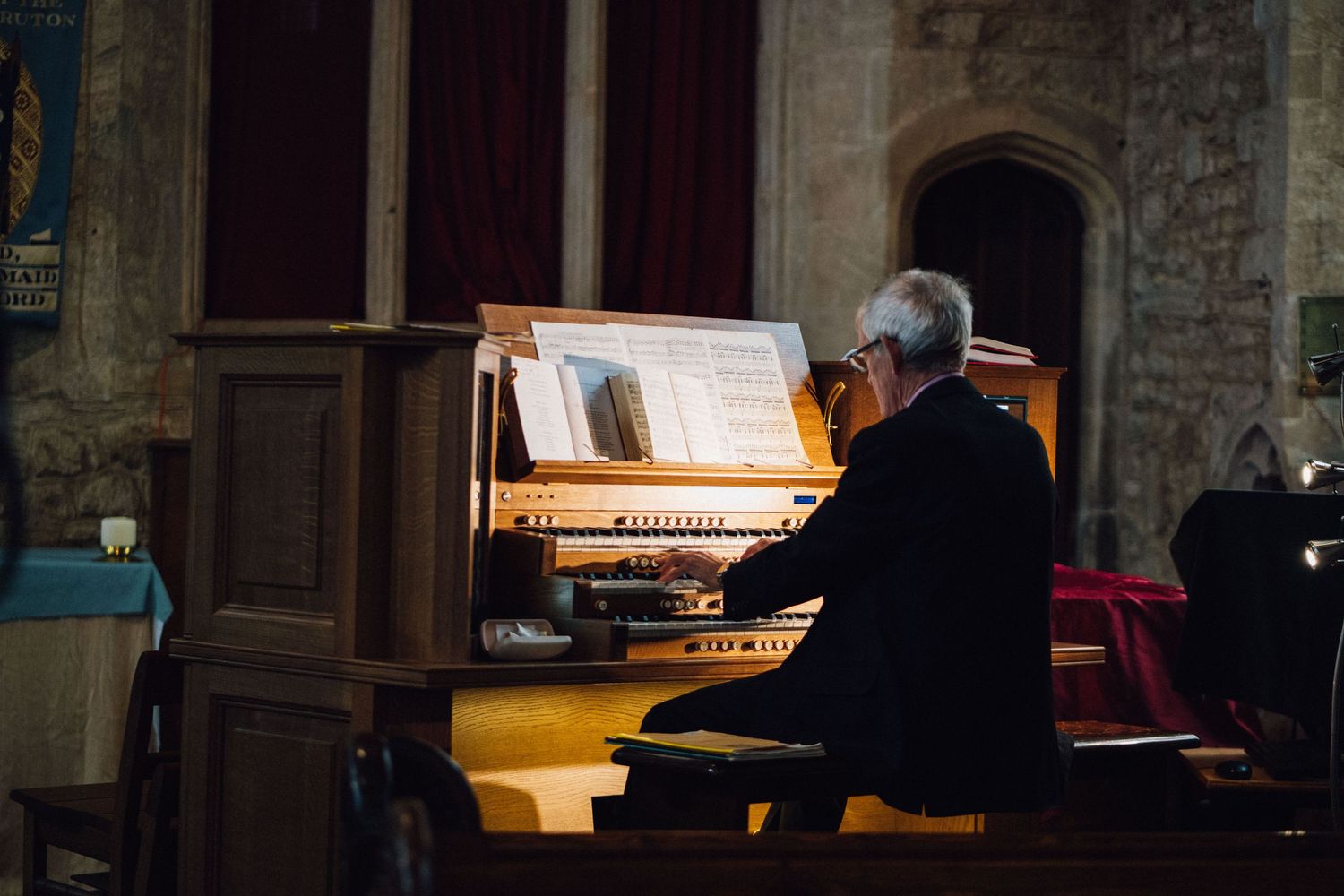 A silhouetted organist performs at a grand pipe organ in a dimly lit cathedral setting.