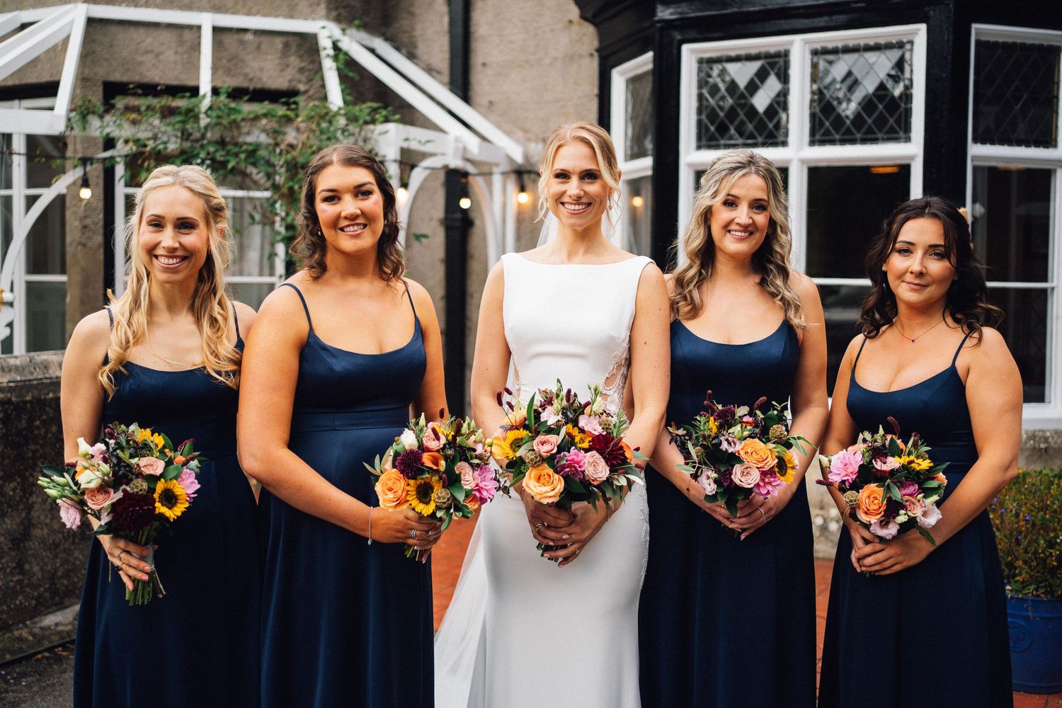 Wedding party members in navy blue dresses holding colorful sunflower bouquets.