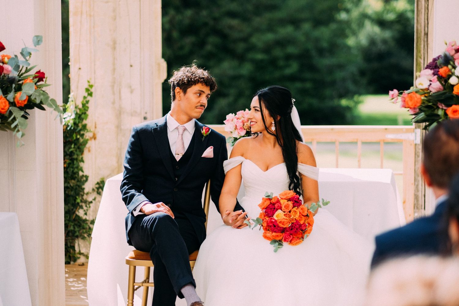 A couple shares a tender moment during their outdoor wedding ceremony surrounded by floral arrangements.