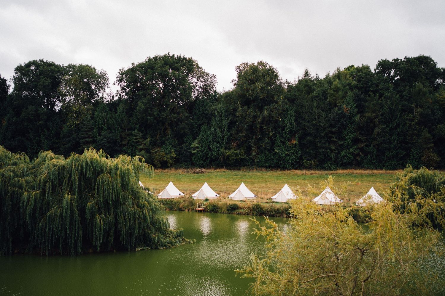 Row of illuminated white bell tents reflected in a tranquil lake at dusk.