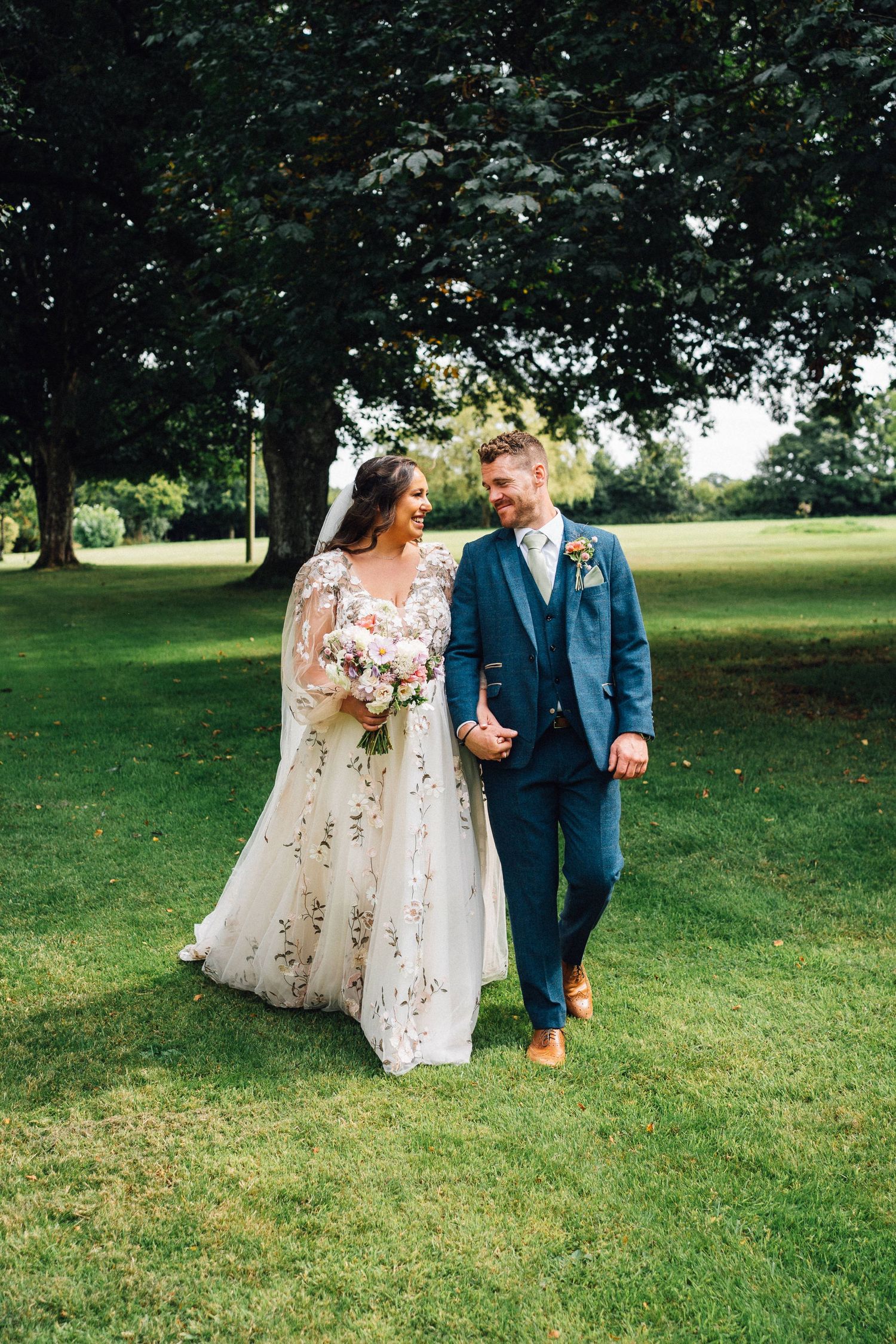Couple strolls together on green lawn during their wedding day.