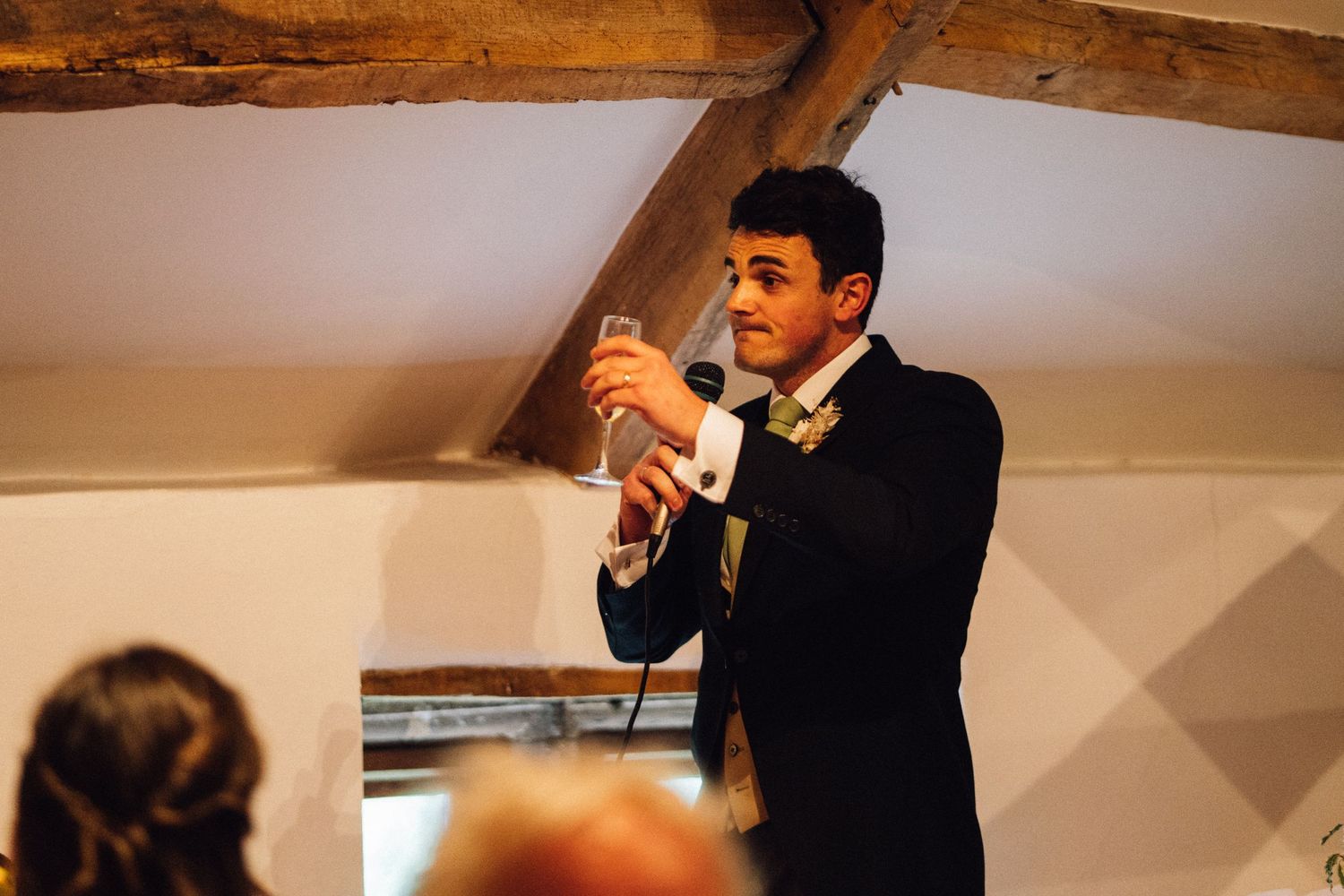 Speech being delivered at an indoor wedding reception under wooden beams.