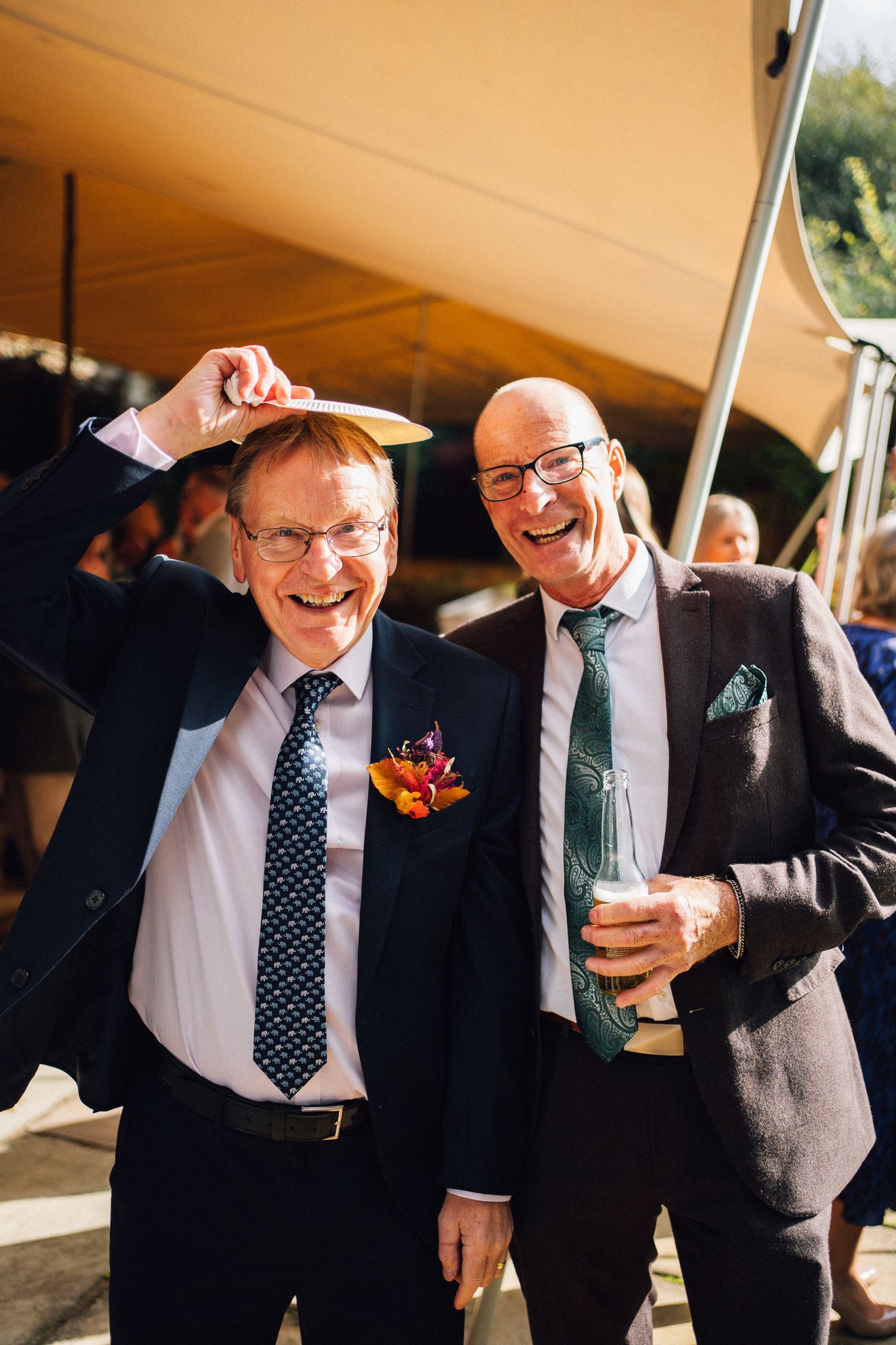 Wedding guests enjoying drinks and conversation under outdoor tent.
