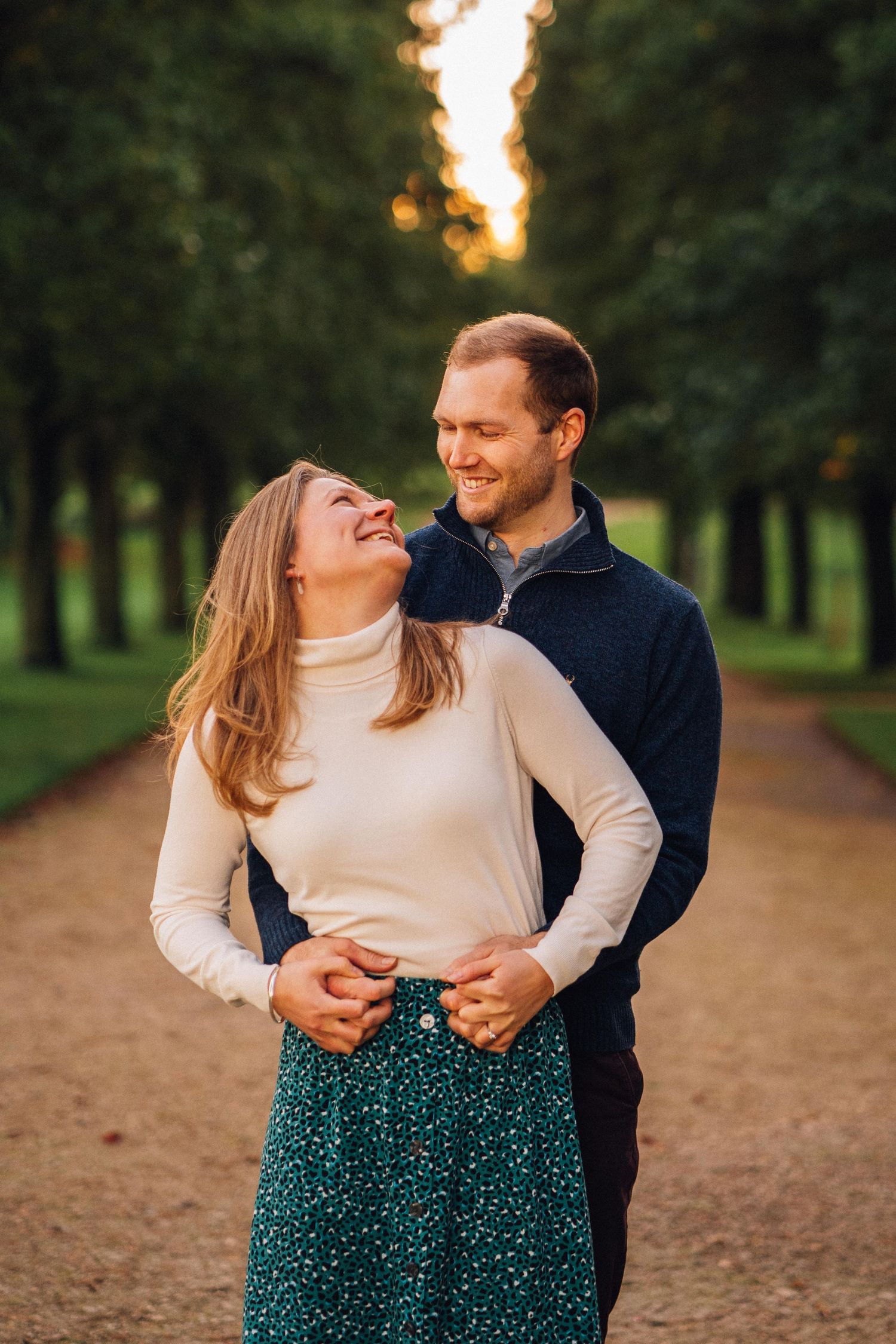 Couple sharing a tender moment on a tree-lined path during sunset.