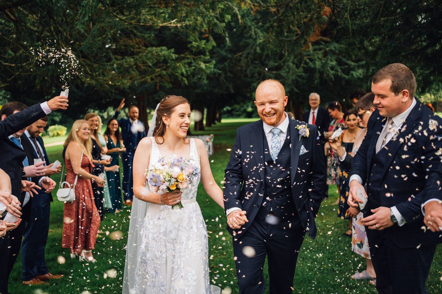 Wedding guests shower the newlyweds with confetti during an outdoor garden celebration.