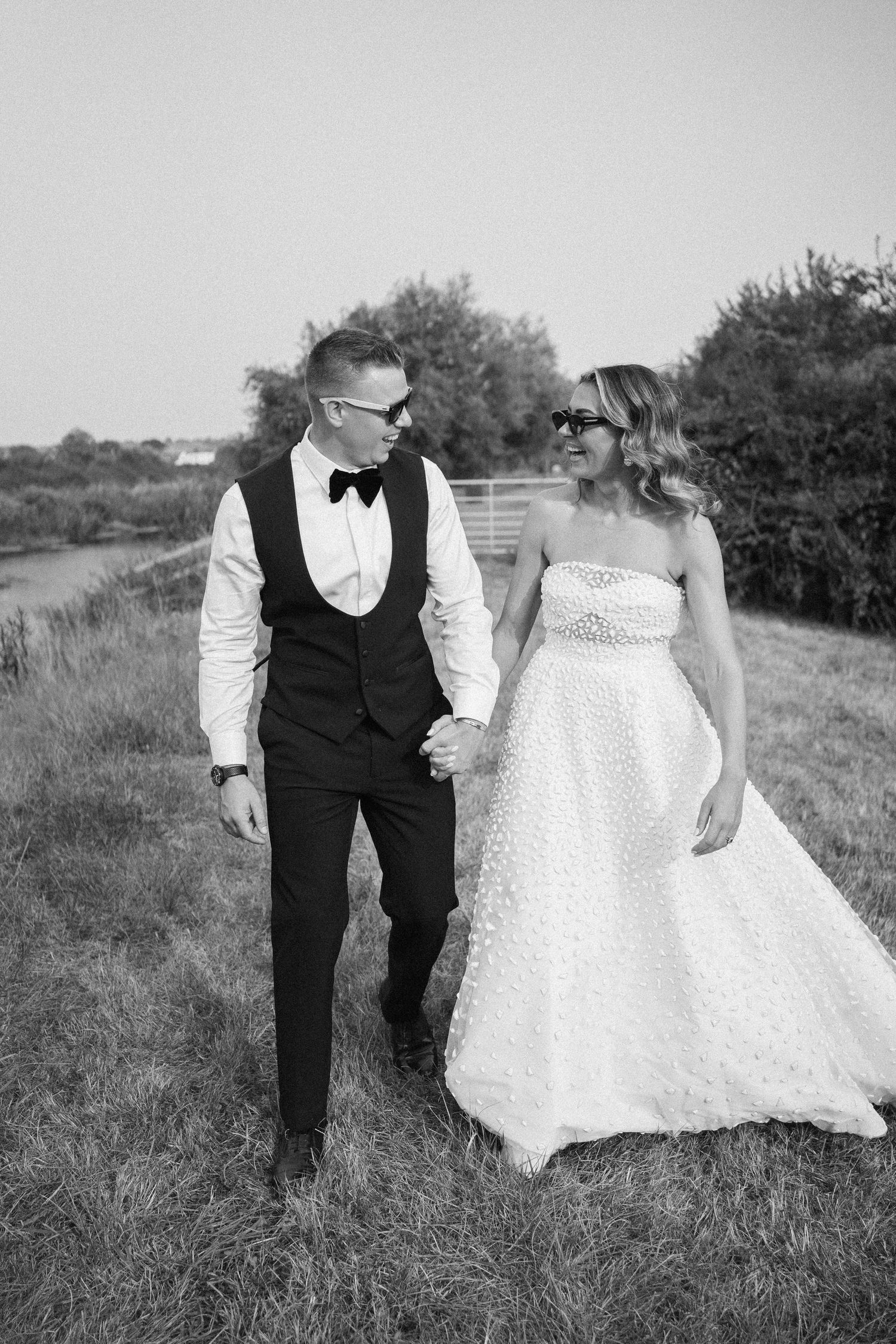 A black and white wedding photo series showing a couple walking together in a grassy field.