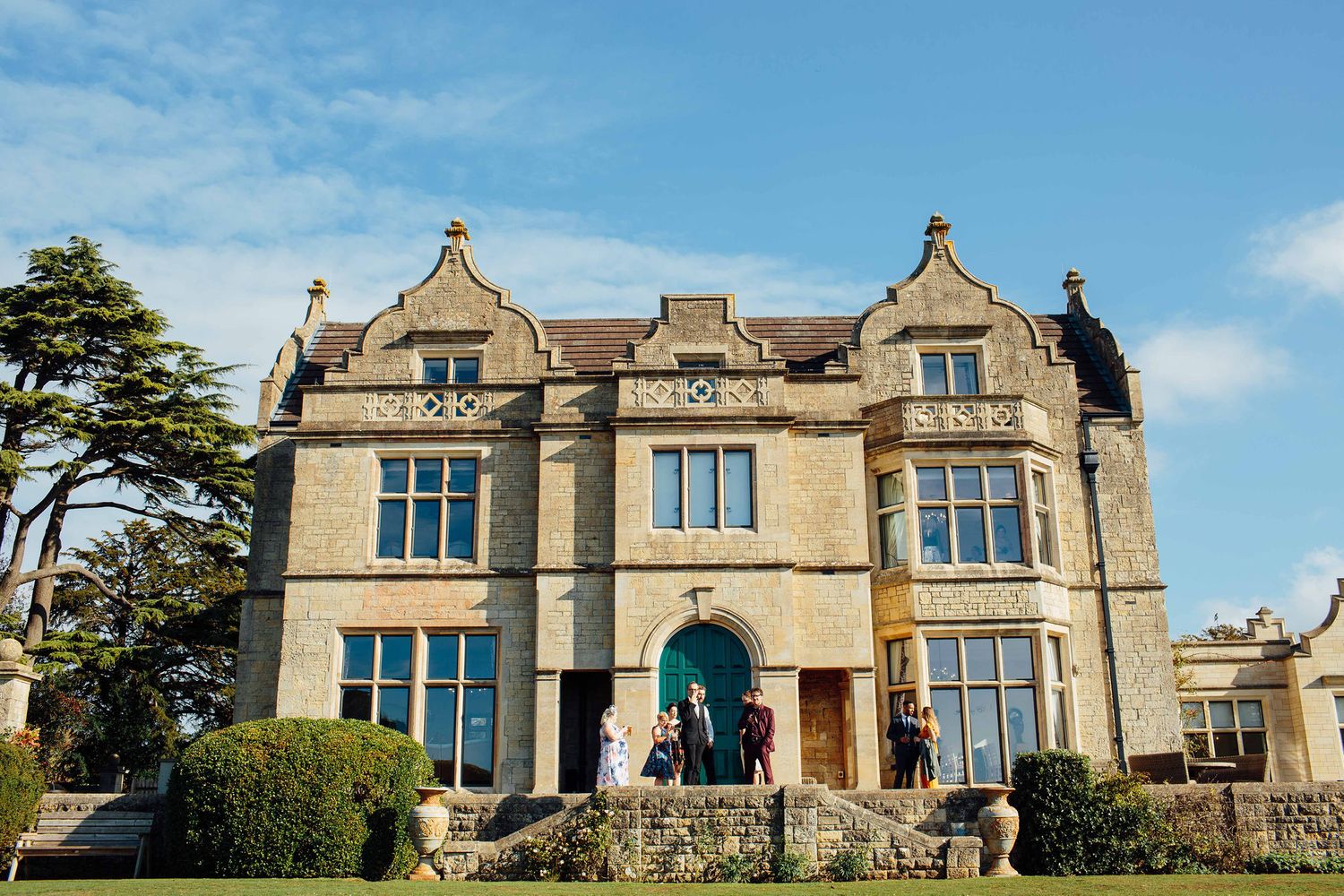 Exterior view of a grand stone manor house with Gothic architectural features under blue sky.