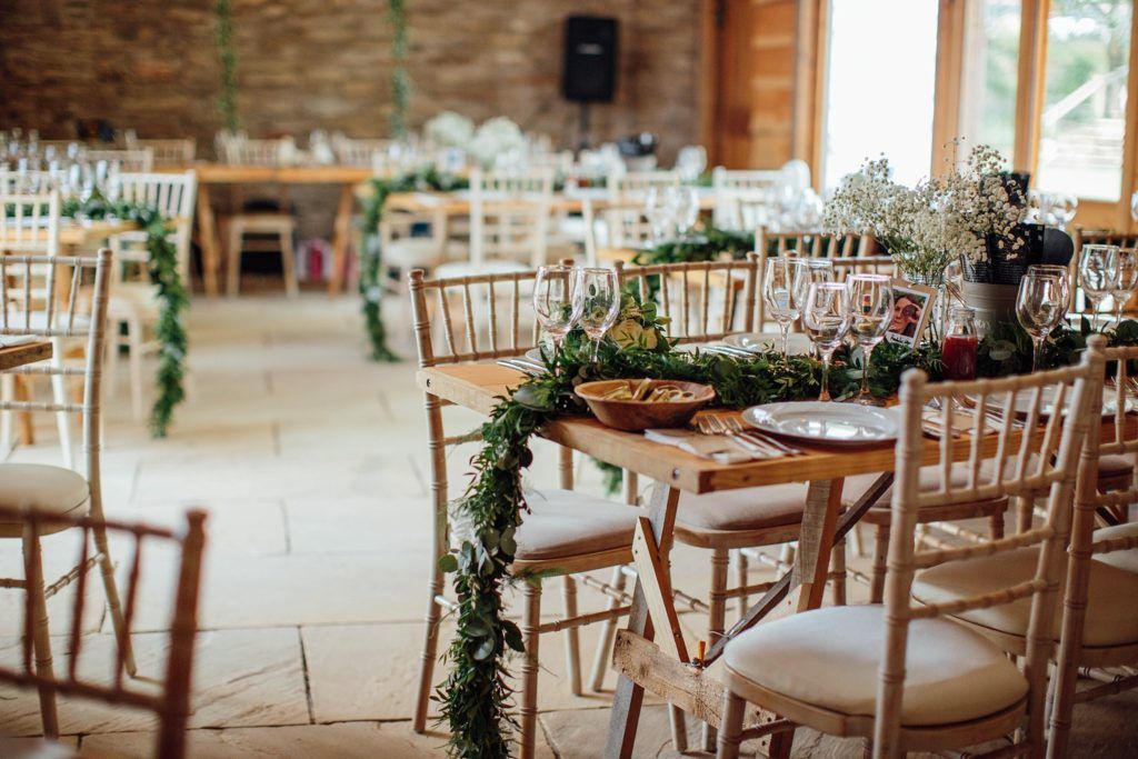 Rustic barn wedding reception venue with wooden beams and elegant table settings decorated with greenery garlands.