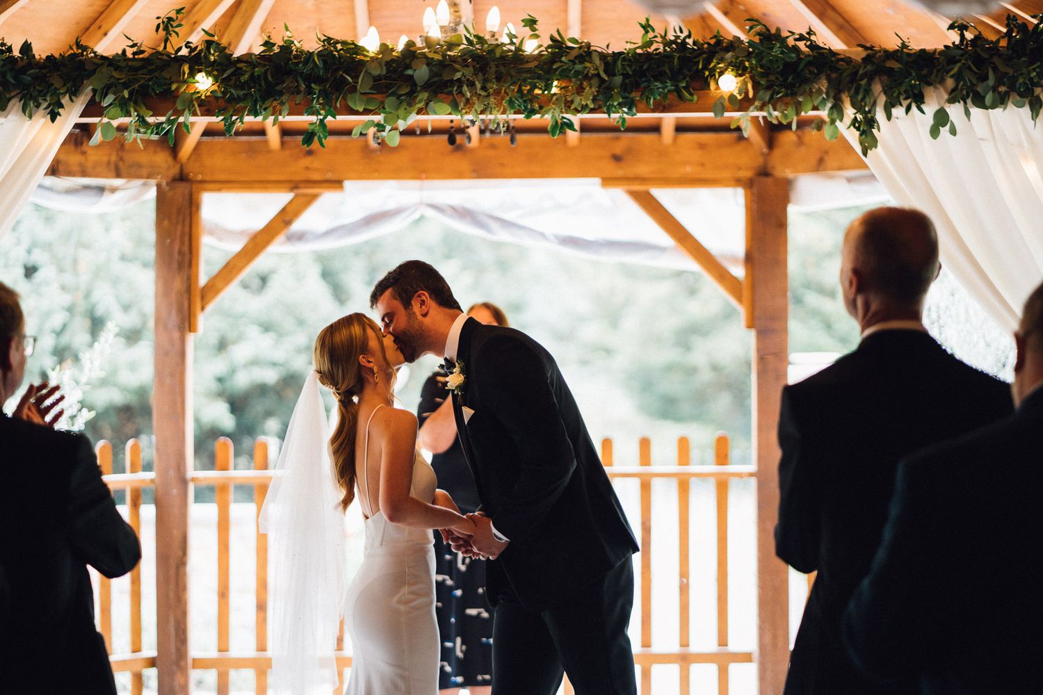 Wedding ceremony silhouettes in a rustic barn setting with natural light streaming through windows.