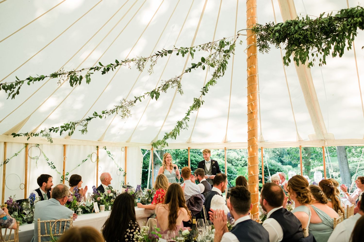 Panoramic view of an outdoor wedding reception tent with elegant white draping and natural decorations.