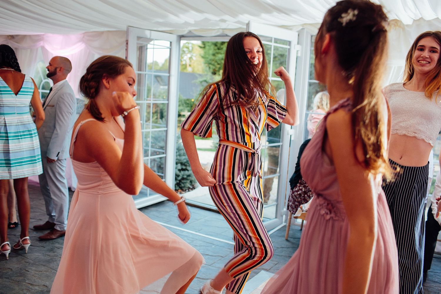 Wedding guests in pink dresses dance and celebrate on the reception dance floor.